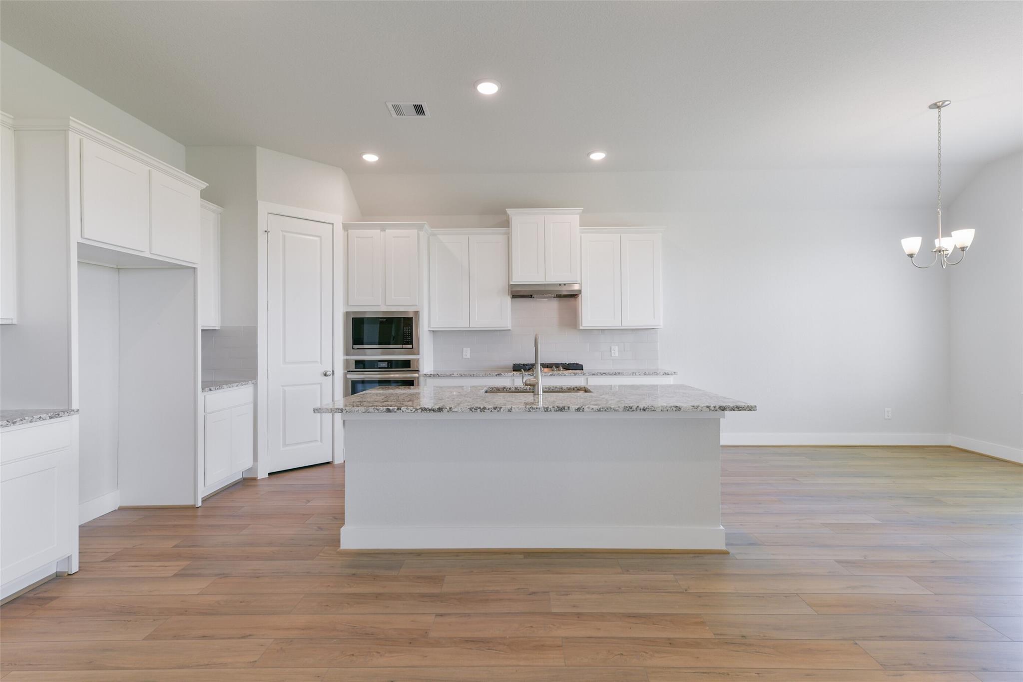 Modern white kitchen with granite island, stainless appliances, and open layout in Davidson Homes The Edward A, Lago Mar, Texas City