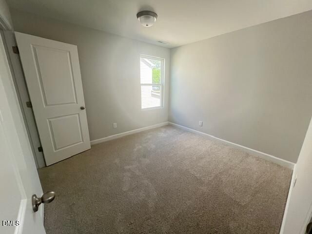 Bright empty bedroom featuring light gray walls, beige carpet, and large window in Davidson Homes The Adalynn A, Lillington, NC