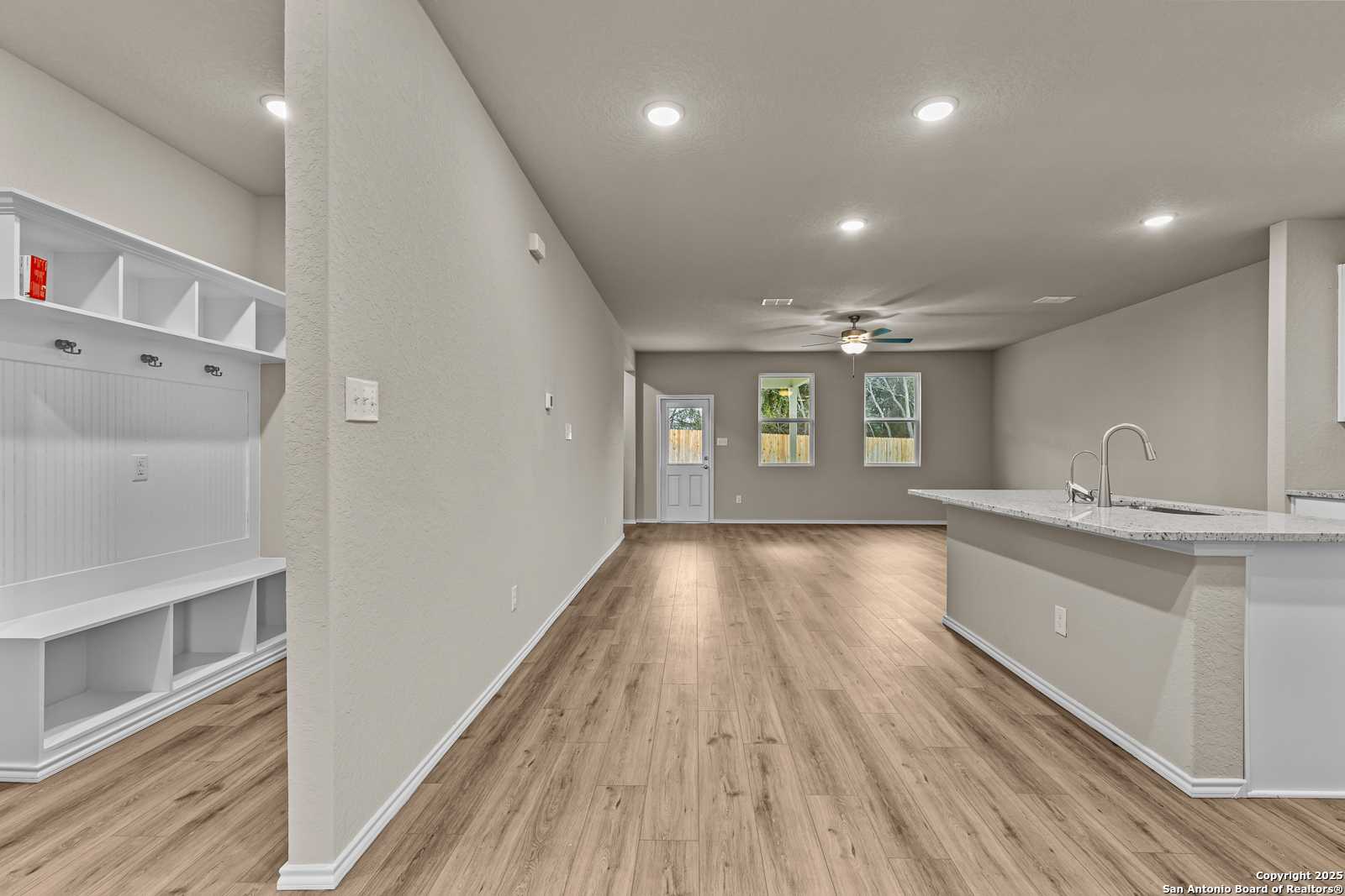 Spacious mudroom with built-in white bench and shelves opening to modern kitchen island in Davidson Homes The Douglas F, San Antonio