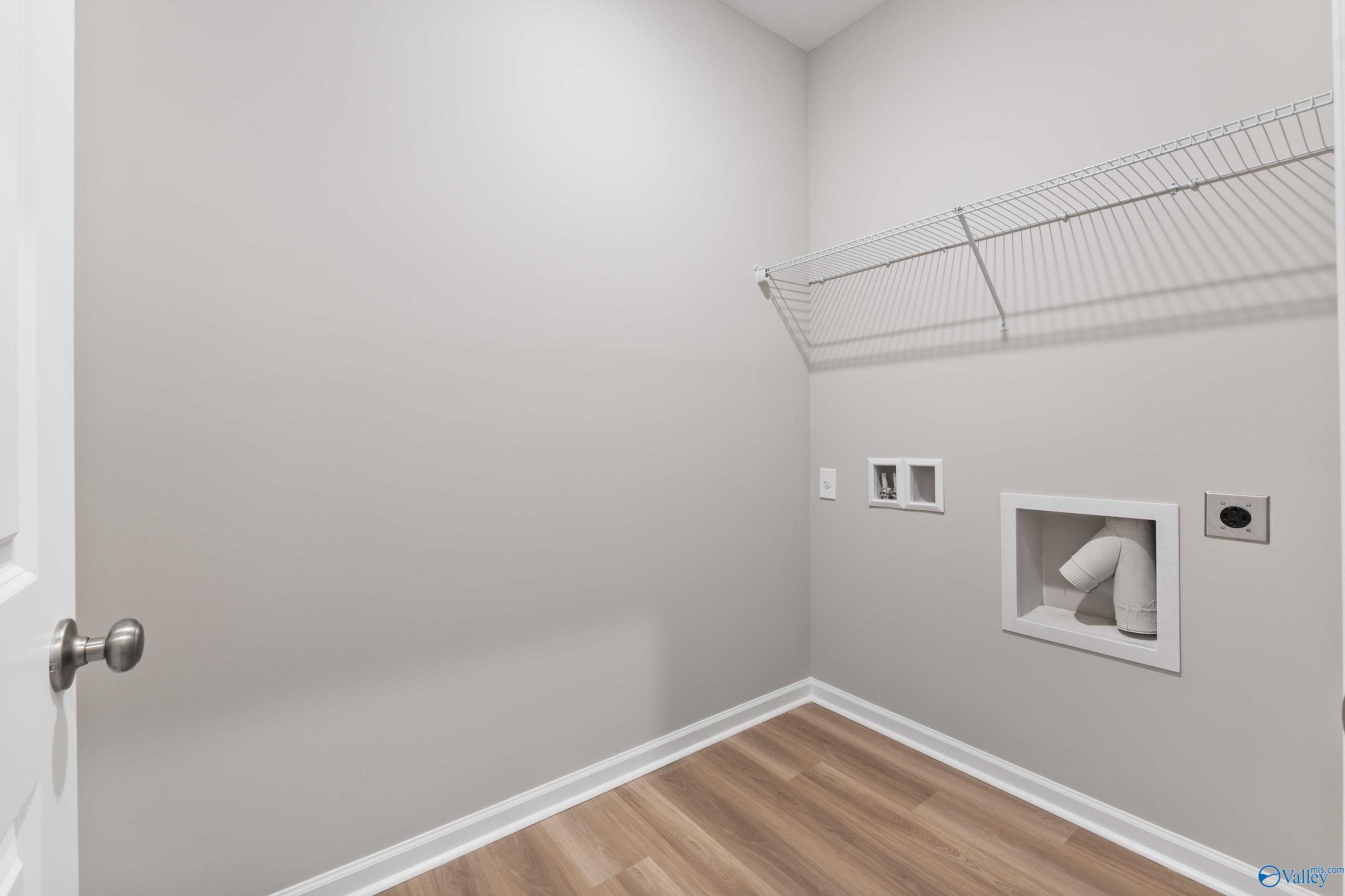 Laundry room with wire shelving, washer/dryer hookups, gray walls, and hardwood floors in The Grace floor plan, Evergreen Mill, Madison AL