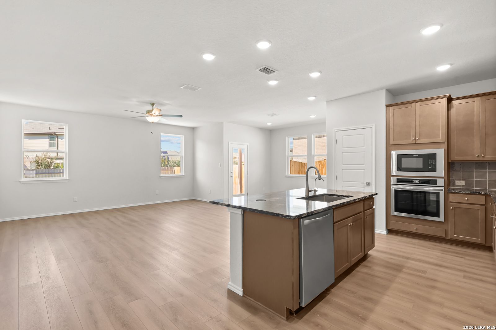 Open-concept kitchen with island, granite countertops, stainless appliances, and wood-look flooring in Davidson Homes Daphne I, San Antonio