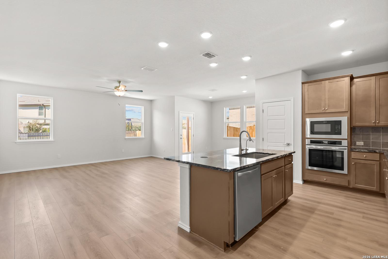 Open-concept kitchen with island, granite countertops, stainless appliances, and wood-look flooring in Davidson Homes Daphne I, San Antonio