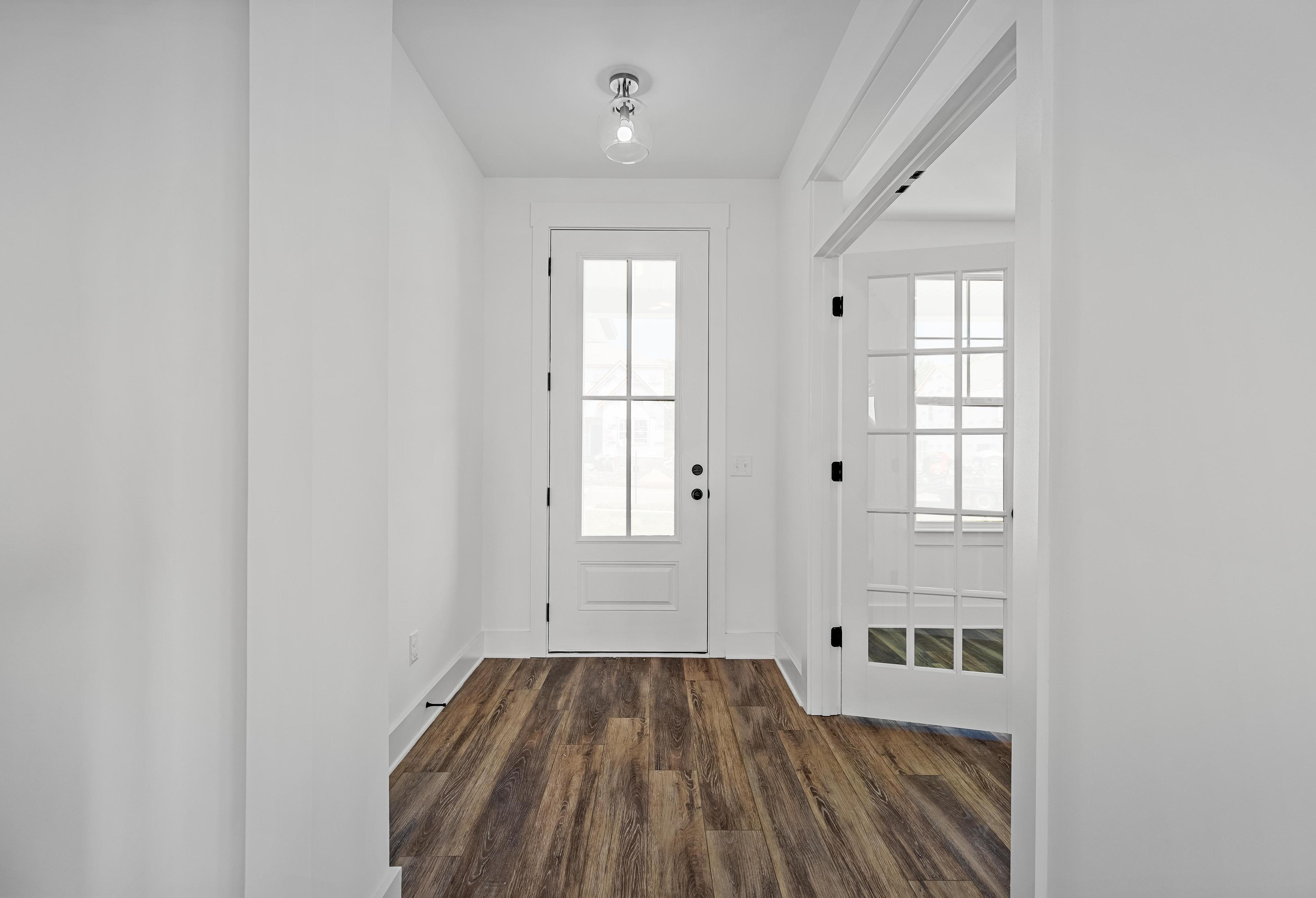 Bright entryway of The Cedar D featuring wood-style flooring, a classic front door, and elegant French doors.