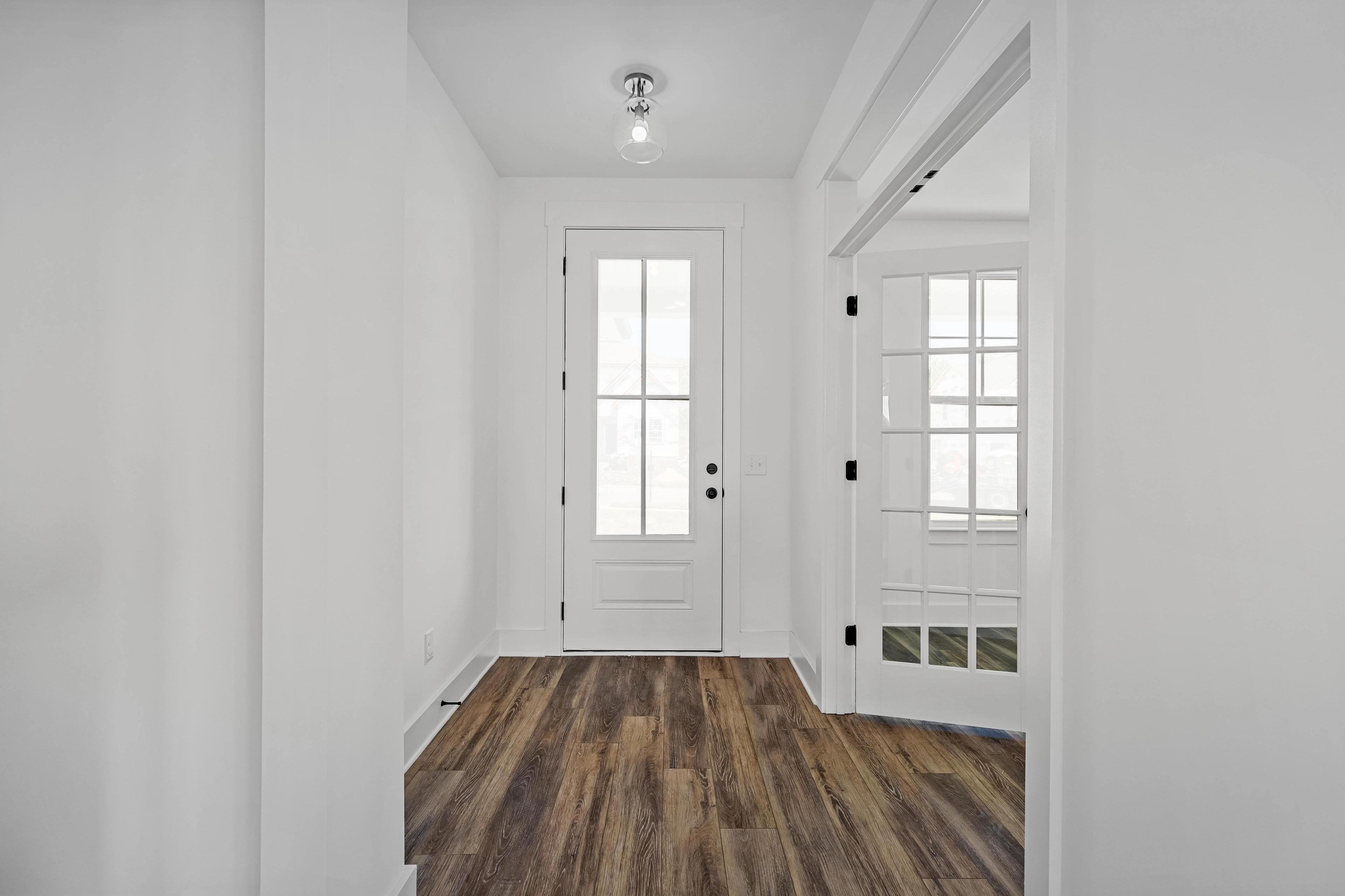 Bright entryway of The Cedar D featuring wood-style flooring, a classic front door, and elegant French doors.