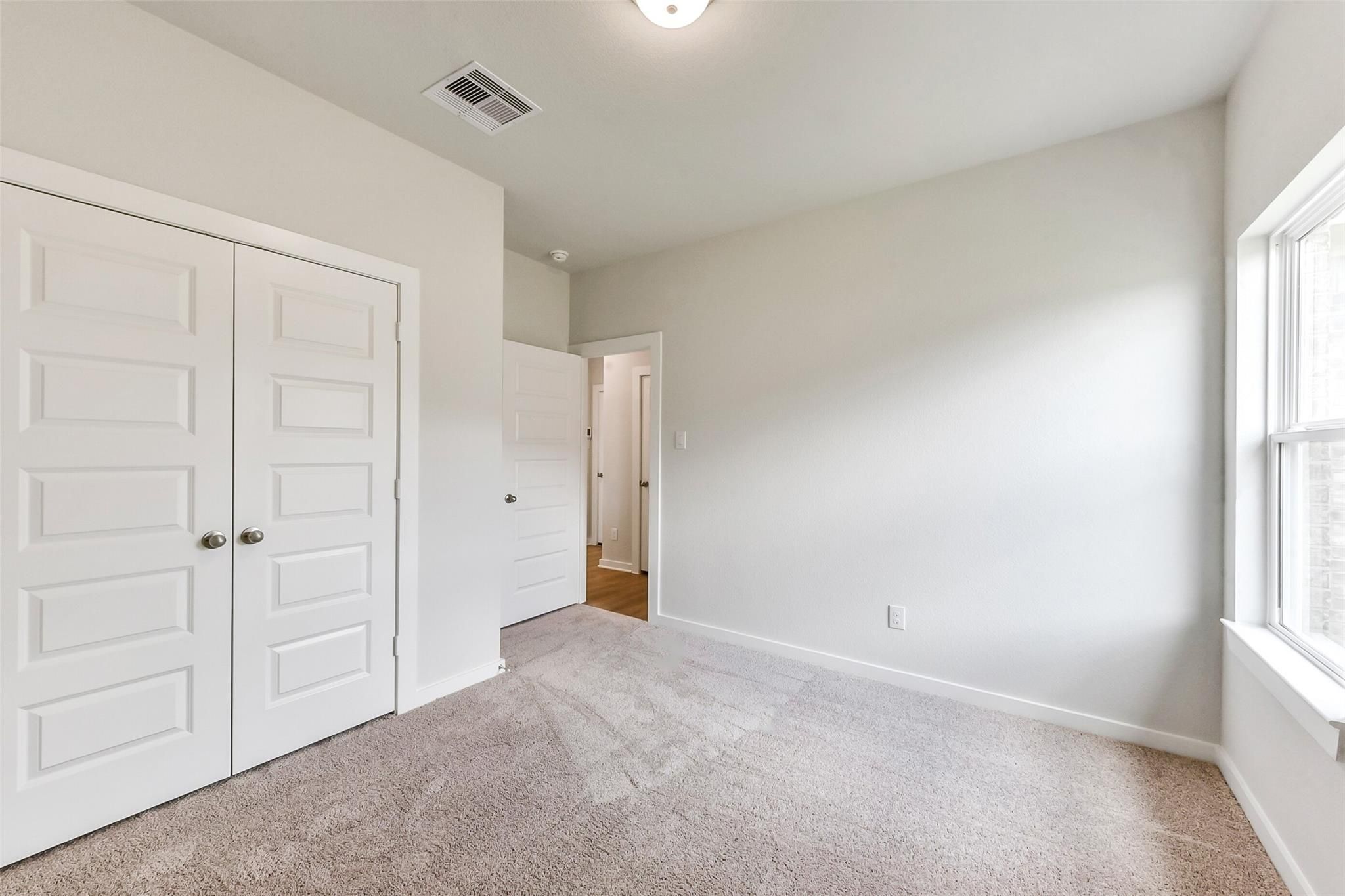 Bright secondary bedroom with beige walls, plush carpet, double closet doors, bath access, and window in Davidson Homes The Costa B, Dayton, Texas