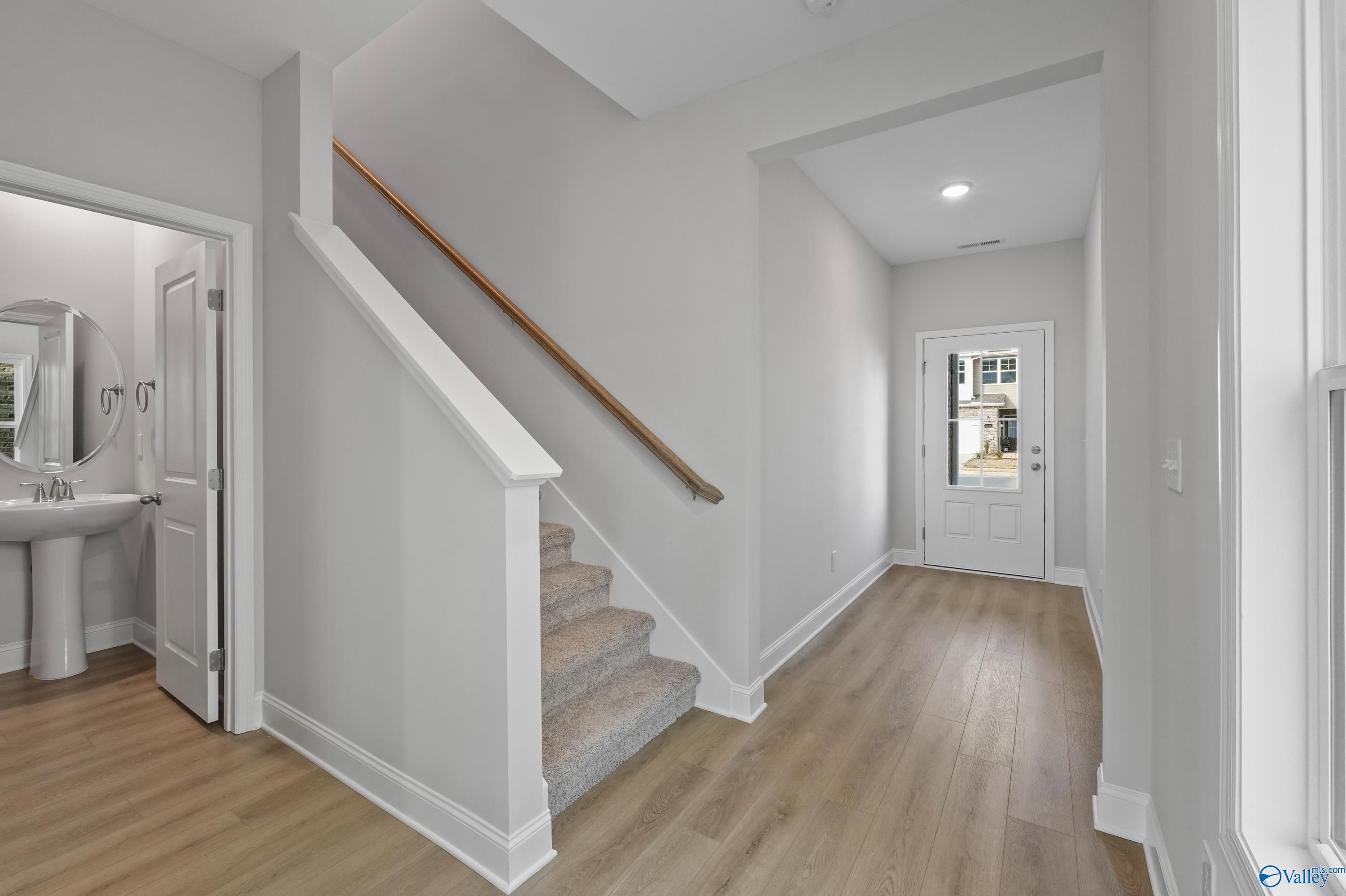 Elegant foyer with carpeted staircase, powder room featuring pedestal sink, and glass-paneled front door in The Camden home, Huntsville, AL