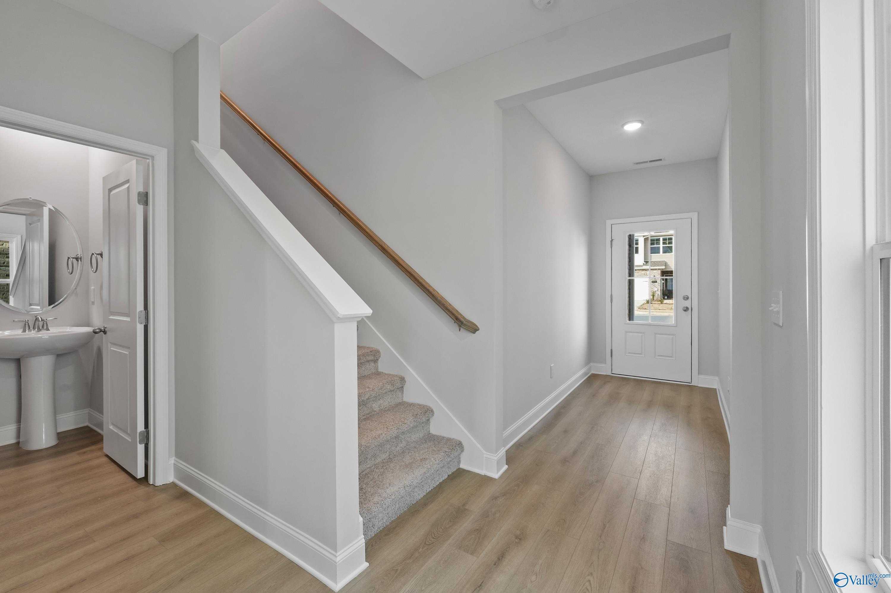 Elegant foyer with carpeted staircase, powder room featuring pedestal sink, and glass-paneled front door in The Camden home, Huntsville, AL