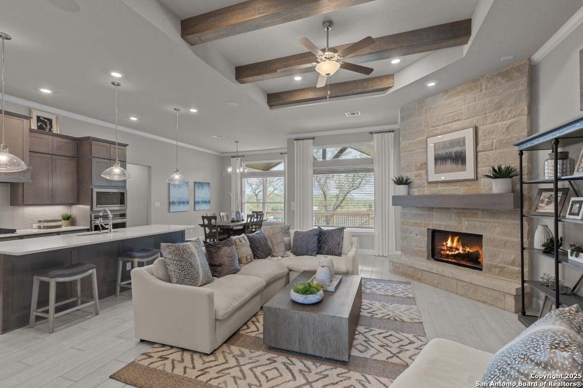 Cozy open-concept living room with stone fireplace, beamed ceiling fan, sectional sofa, and kitchen island in Davidson Homes The Garner B, Ladera, San Antonio
