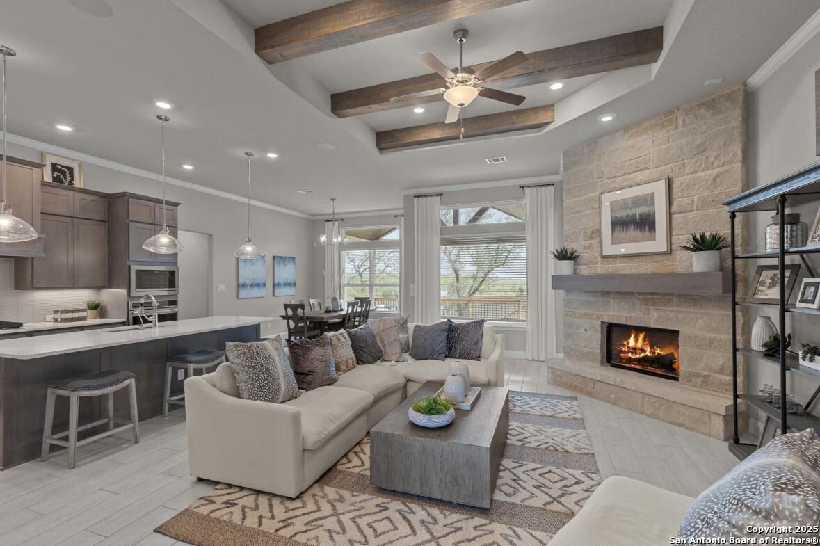 Open-concept living room with stone fireplace, beige sectional sofa, and modern kitchen island in Davidson Homes The Garner B, Ladera, San Antonio