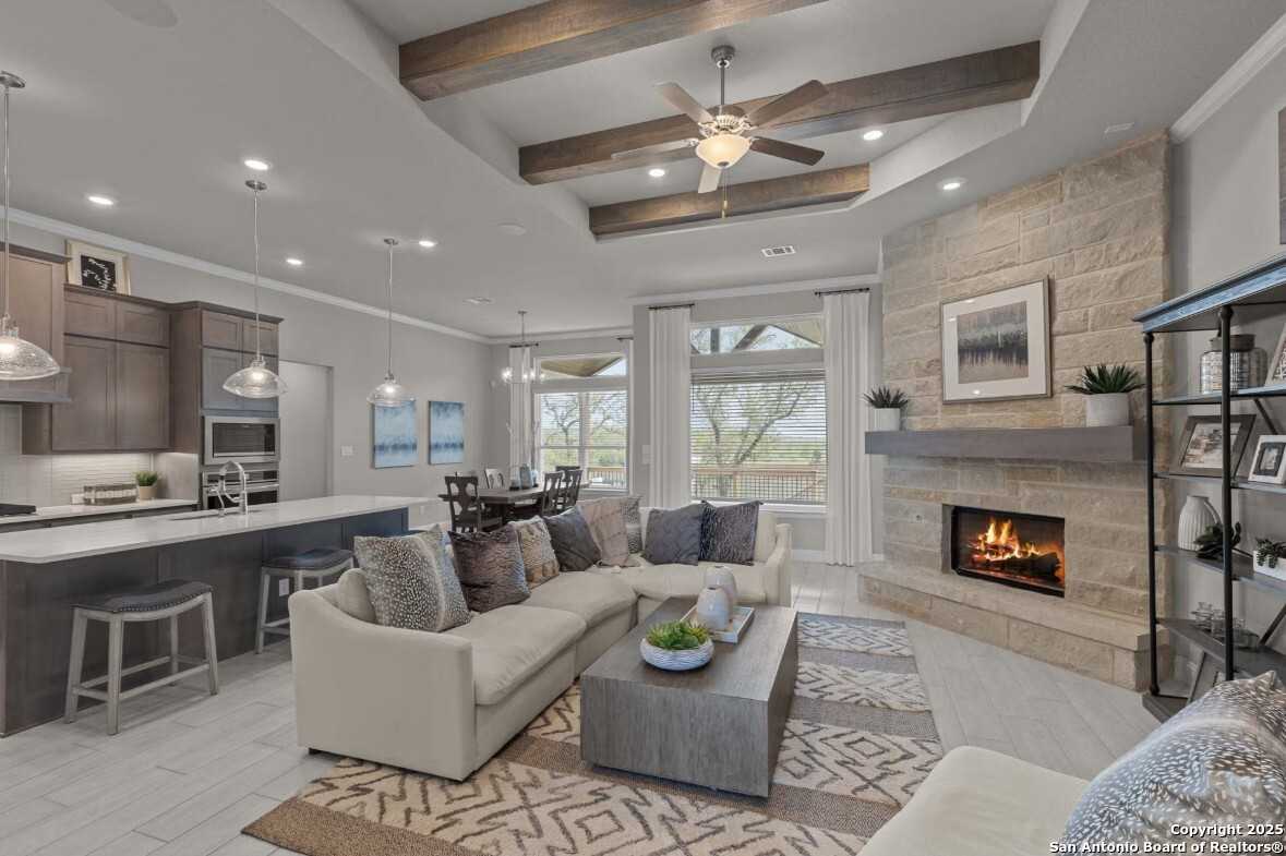 Cozy open-concept living room with stone fireplace, beamed ceiling fan, sectional sofa, and kitchen island in Davidson Homes The Garner B, Ladera, San Antonio