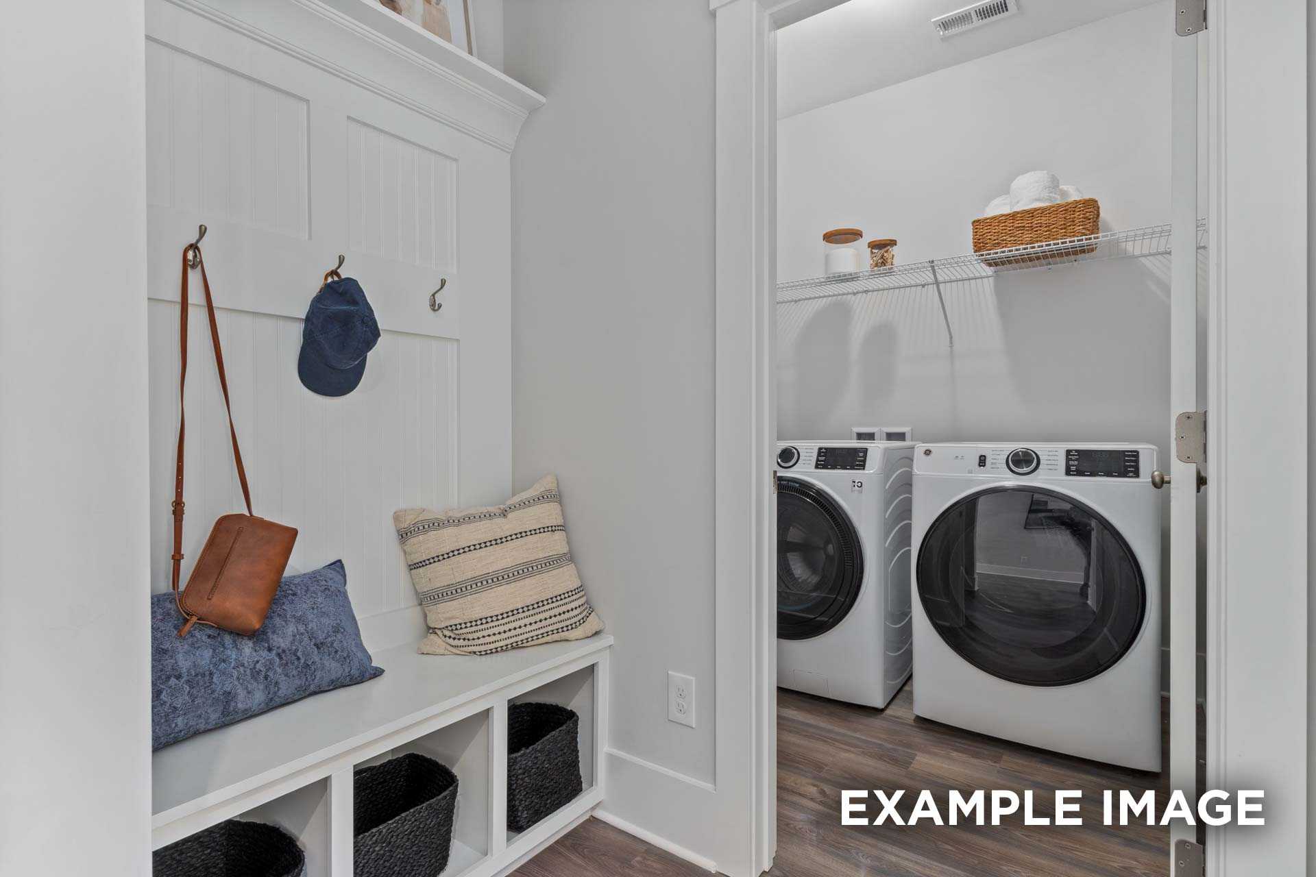 Functional mudroom laundry in The Franklin C home featuring white cabinetry, hooks with purse and hat, cushioned bench, baskets, and stacked washers dryers