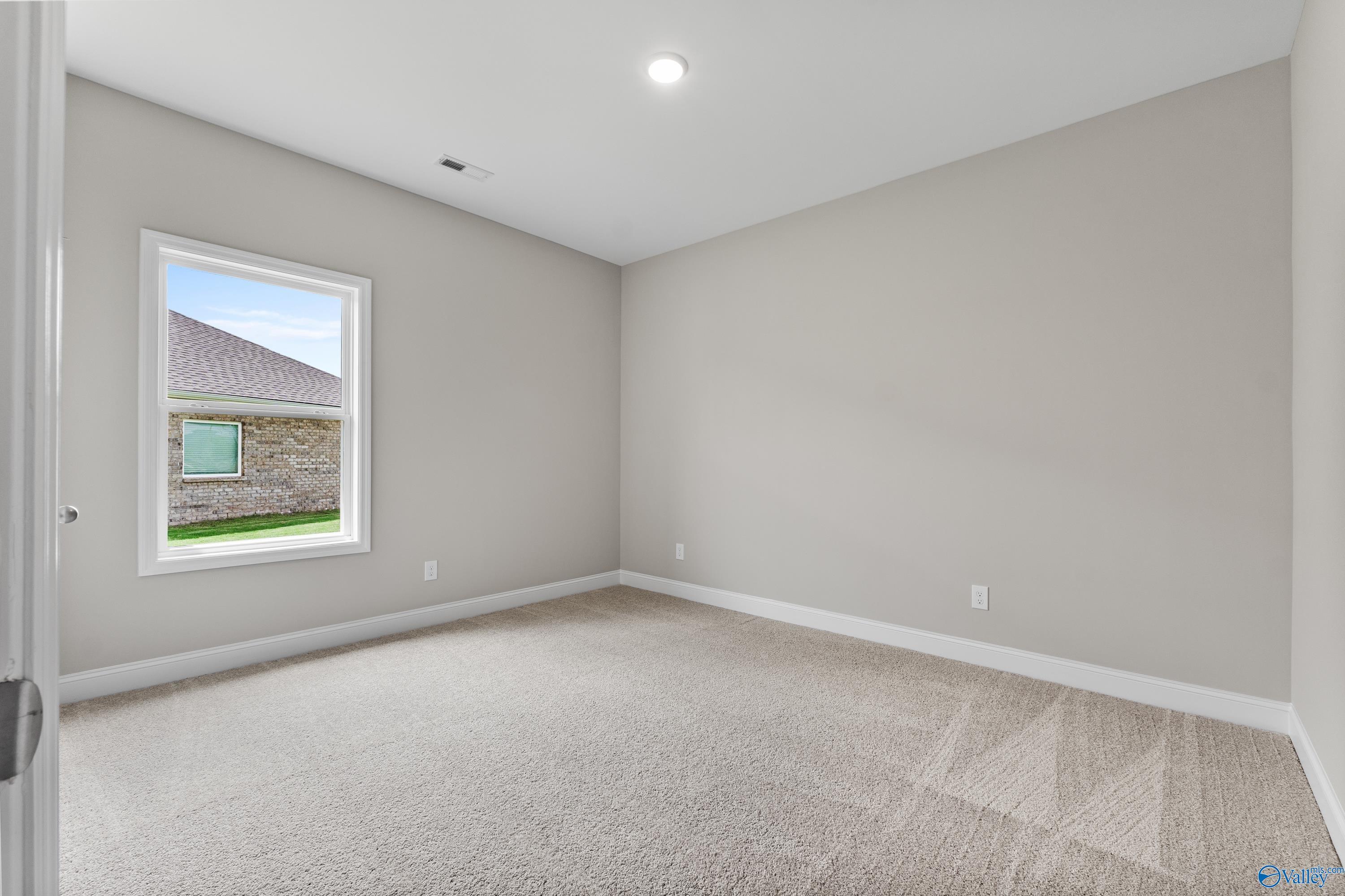 Spacious empty bedroom with light gray walls, beige carpet, and window view in Davidson Homes The Daphne C, Harvest, Alabama