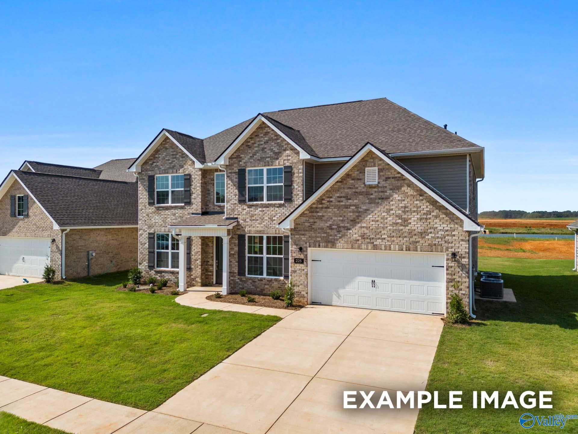 Modern brick 1.5-story home with 2-car garage, covered porch, and lush lawn in Kendall Downs, Toney, Alabama