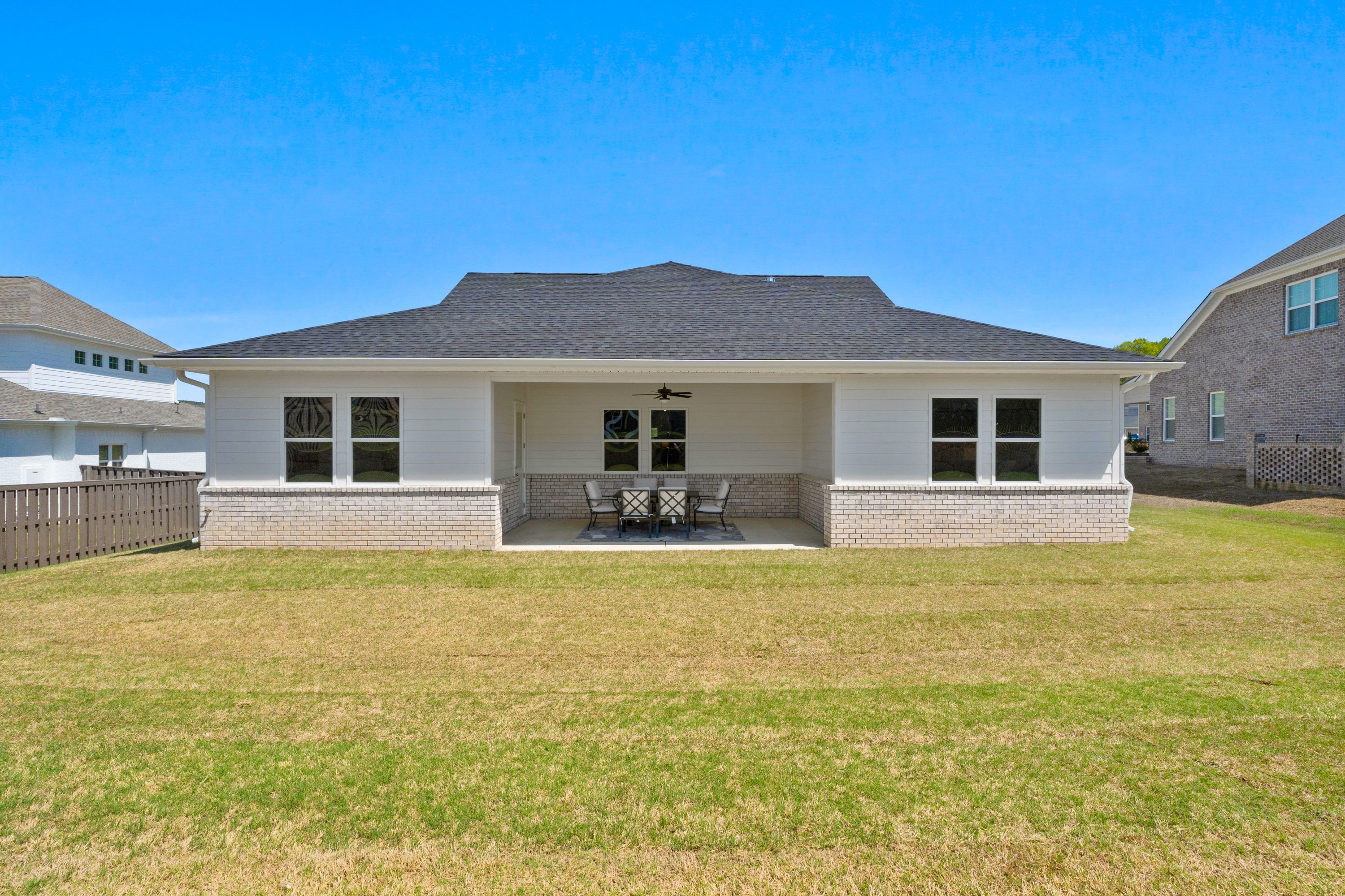 Rear elevation of The Haven D single-story home featuring covered patio with fan, table, chairs, and lush green backyard