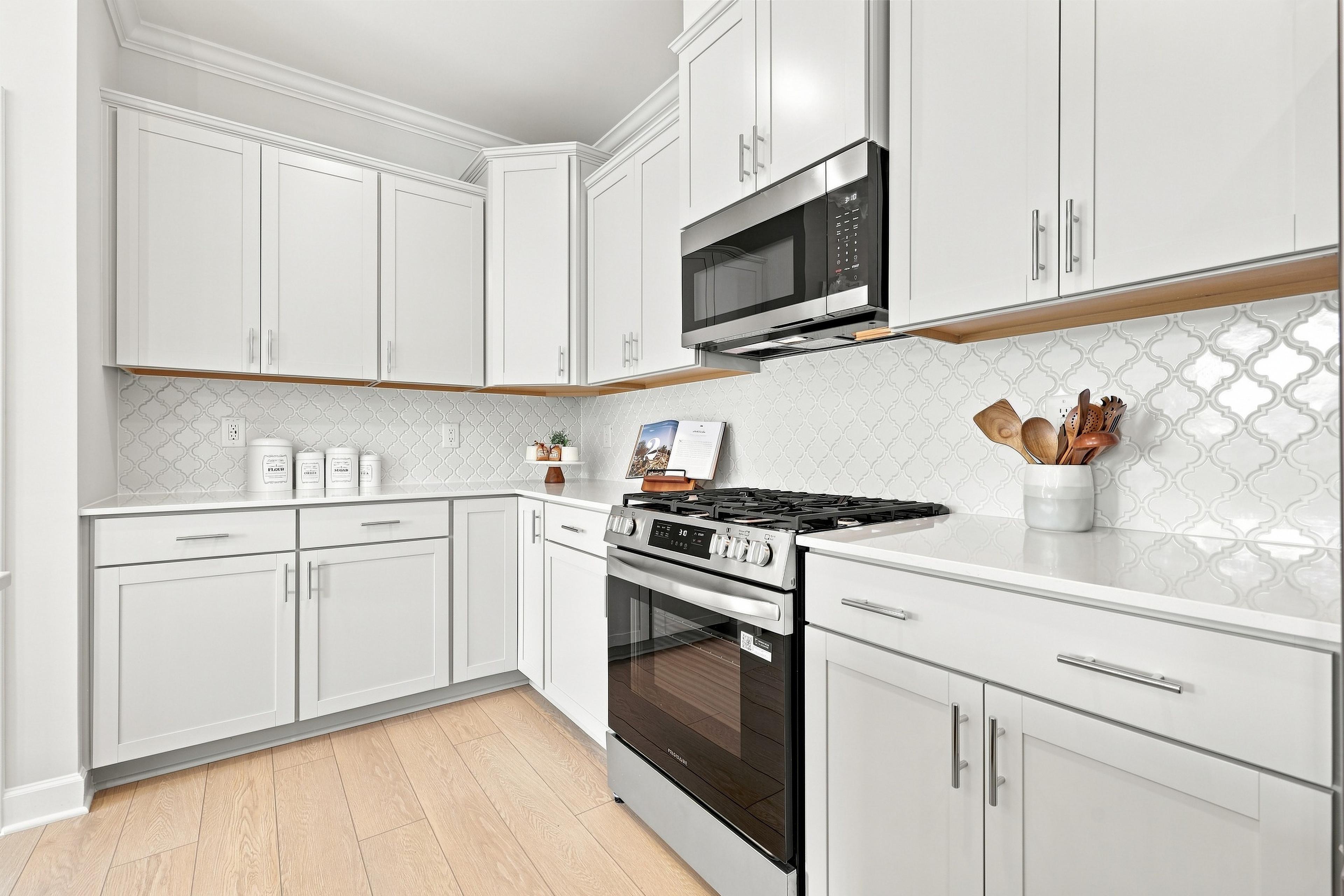 Modern kitchen in The Daphne featuring white shaker cabinets, stainless steel appliances, and elegant arabesque tile backsplash.