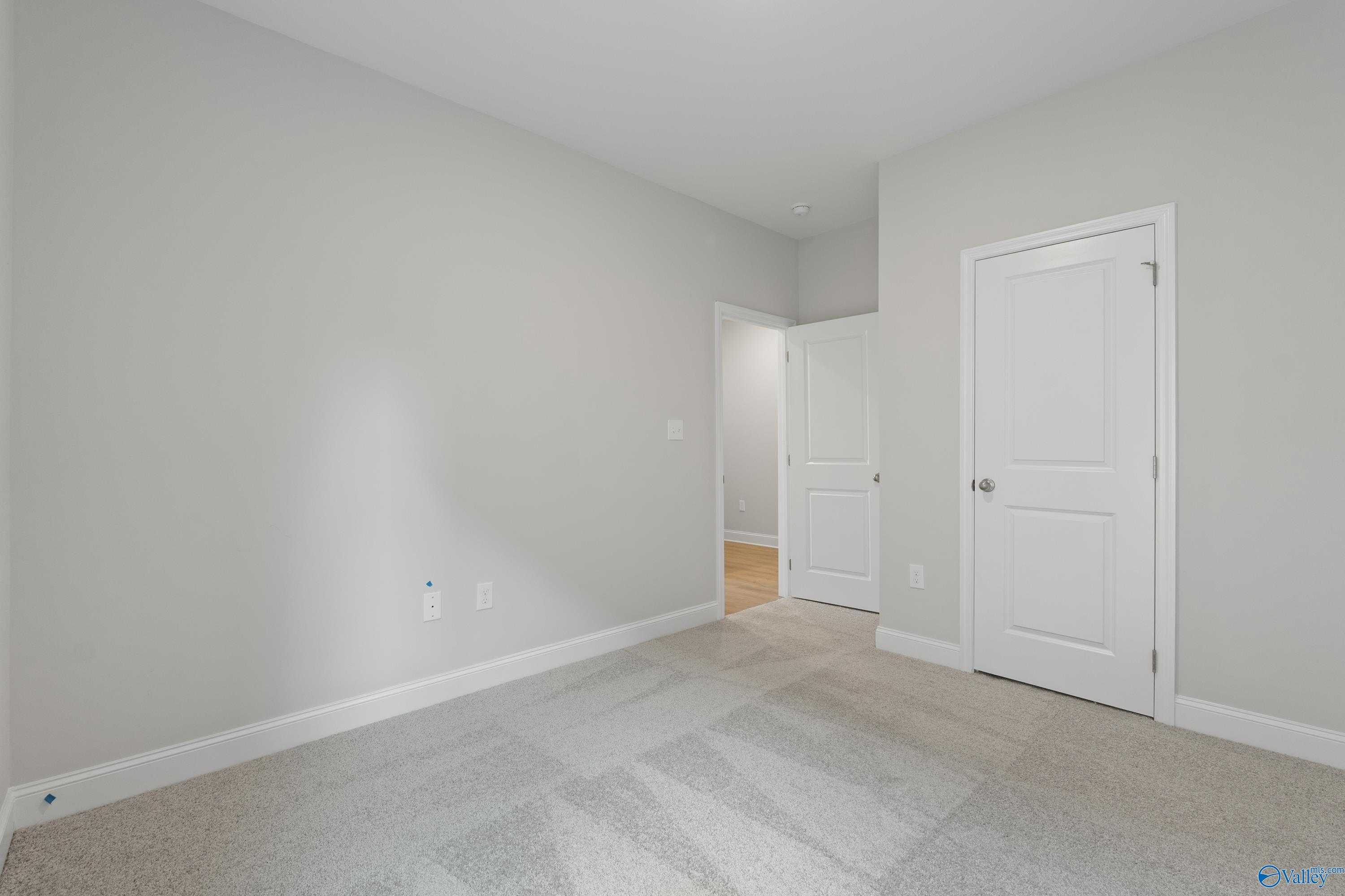 Spacious bedroom with light gray walls, white doors, and beige carpet in The Asheville C floor plan, Davidson Homes, Huntsville, AL