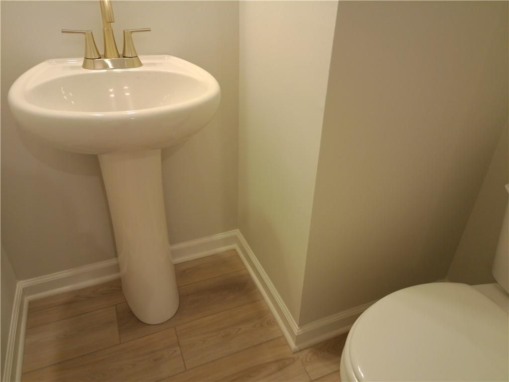 Elegant powder room featuring white pedestal sink, gold faucets, and toilet in Davidson Homes The Marion C, Winder, Georgia