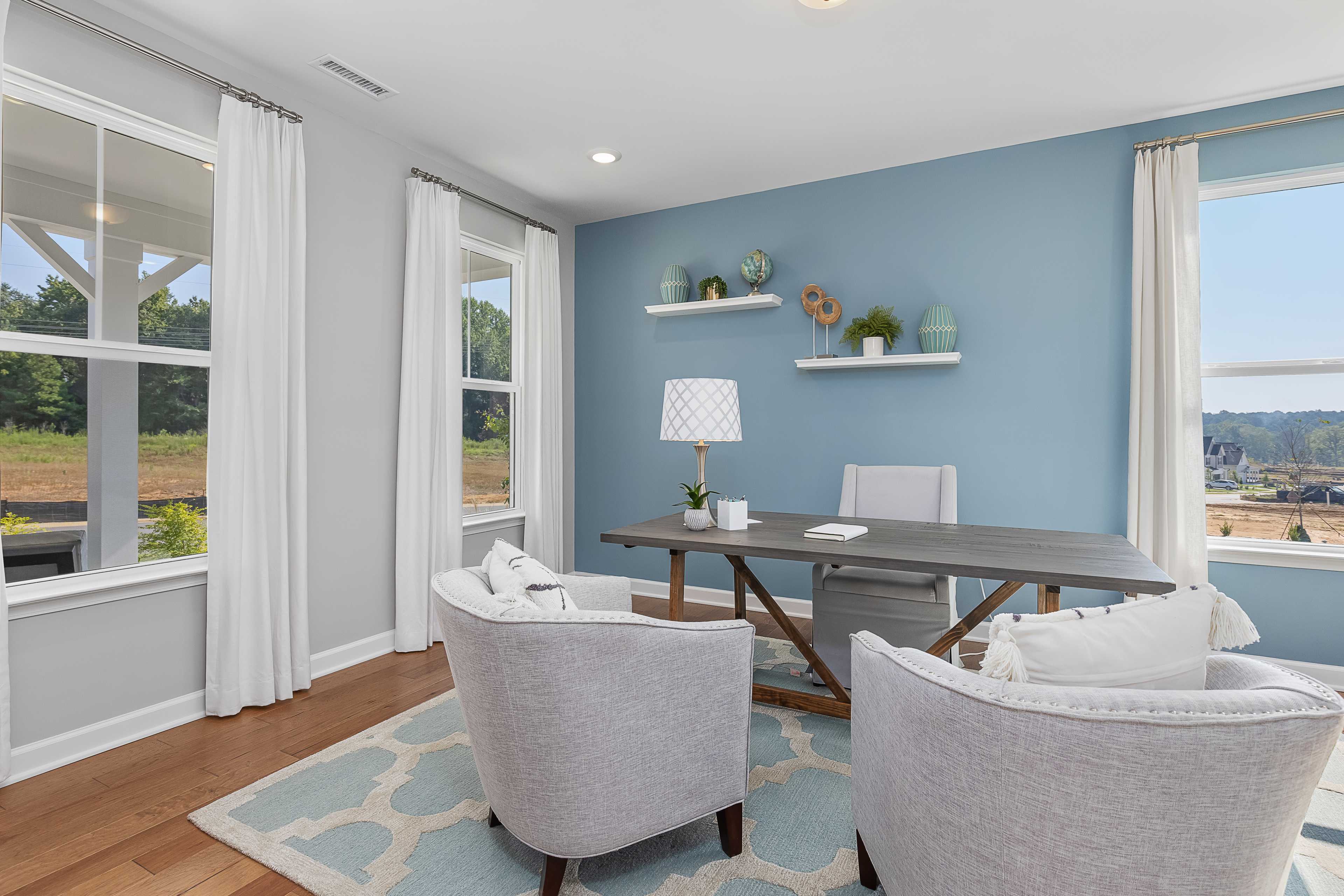 Cozy home office at Woodland Crossing in Zebulon NC featuring wooden desk, blue walls, armchairs, and scenic wooded views