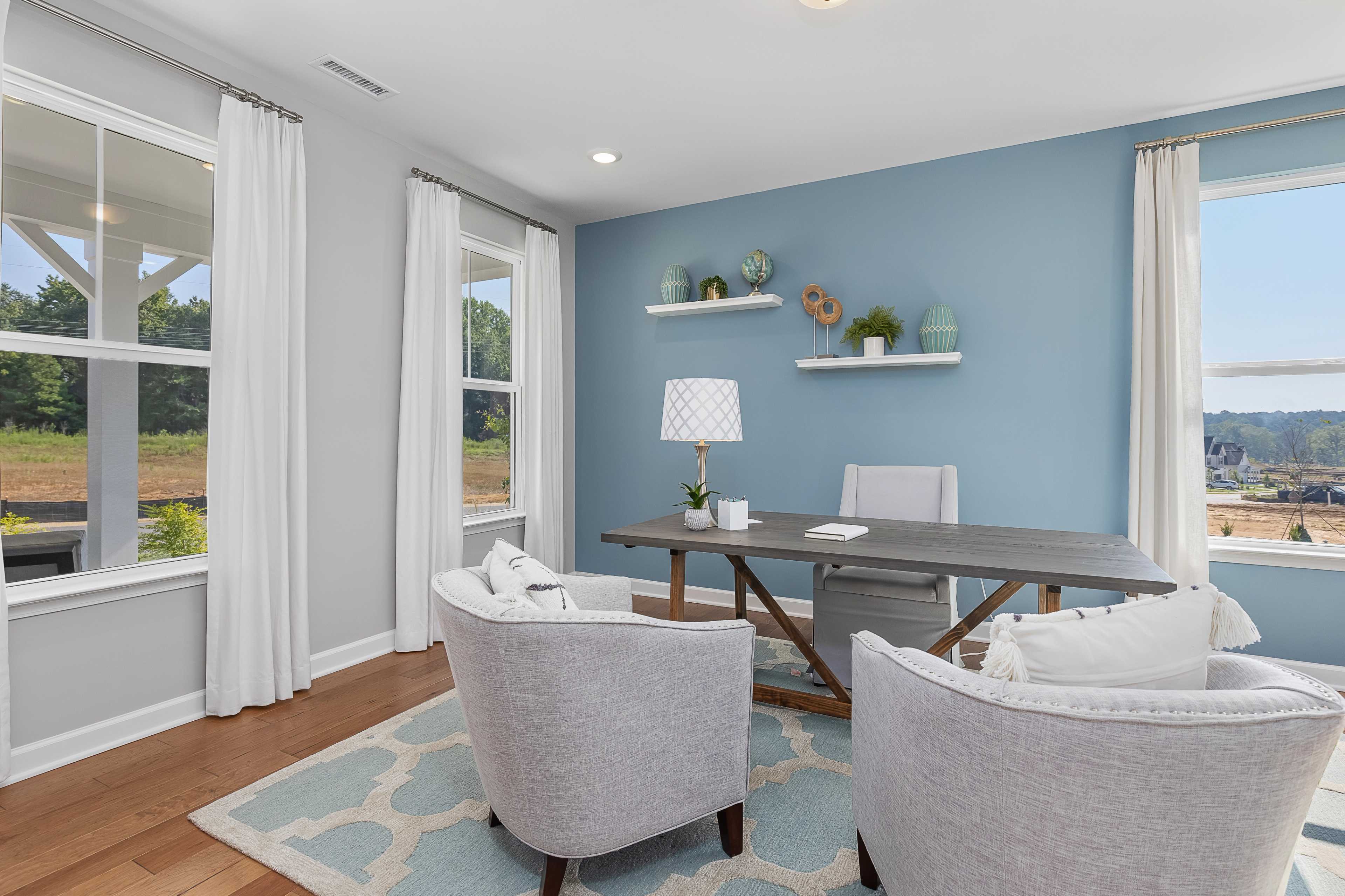 Cozy home office at Woodland Crossing in Zebulon NC featuring wooden desk, blue walls, armchairs, and scenic wooded views