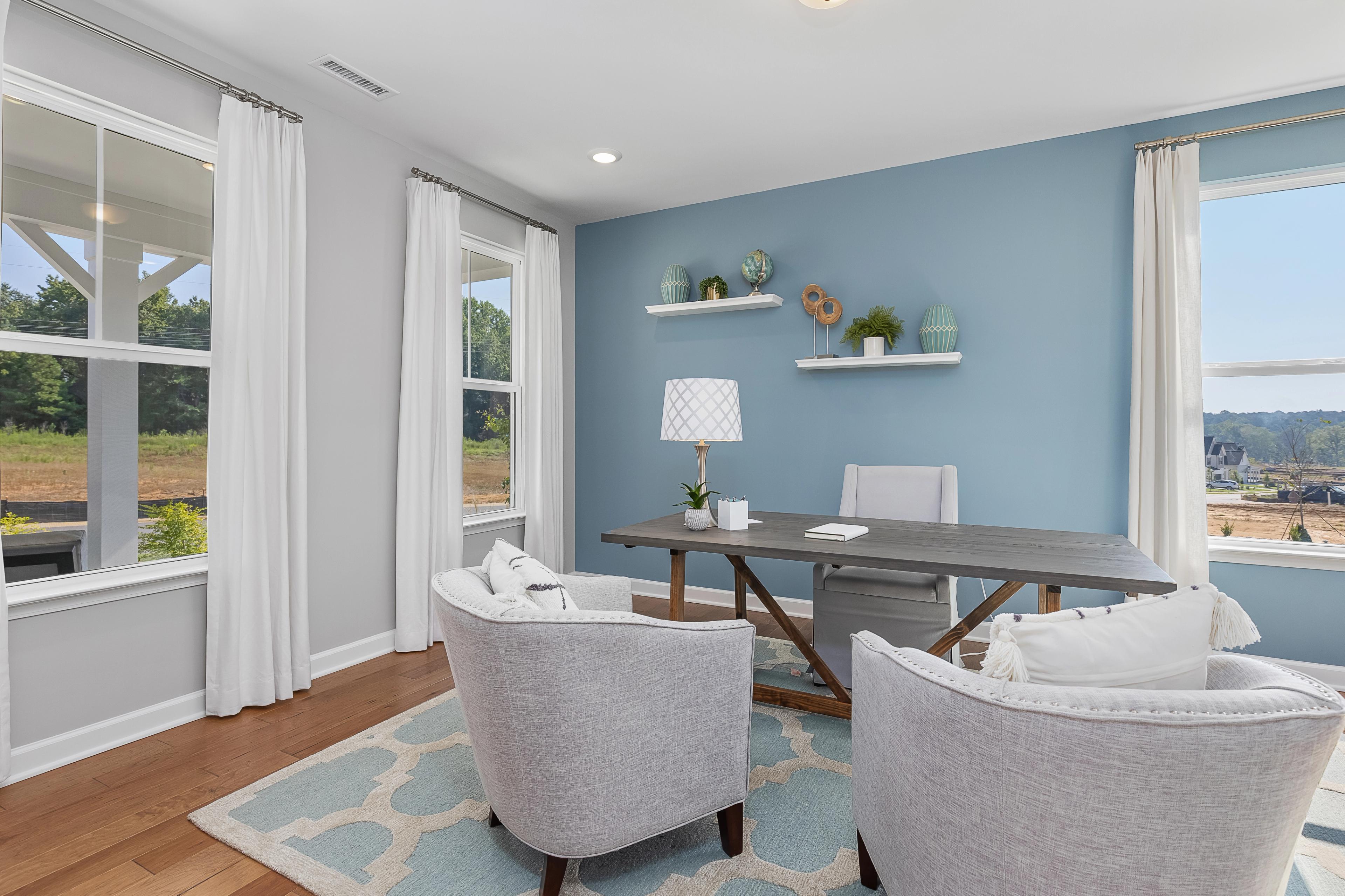 Cozy home office at Woodland Crossing in Zebulon NC featuring wooden desk, blue walls, armchairs, and scenic wooded views