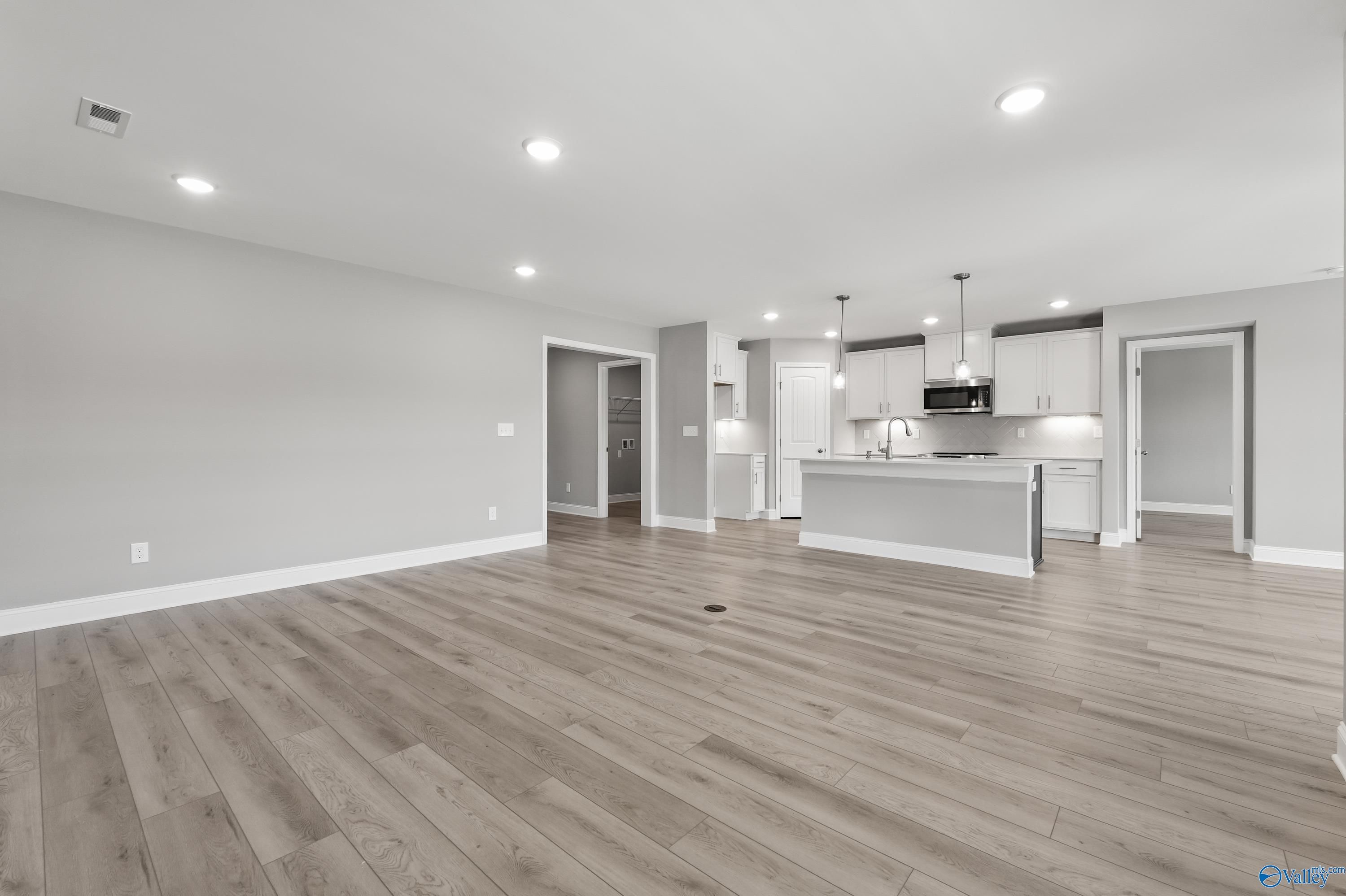 Open-concept kitchen and living space with white cabinets, stainless appliances, hardwood floors in The Everett B, Athens, AL