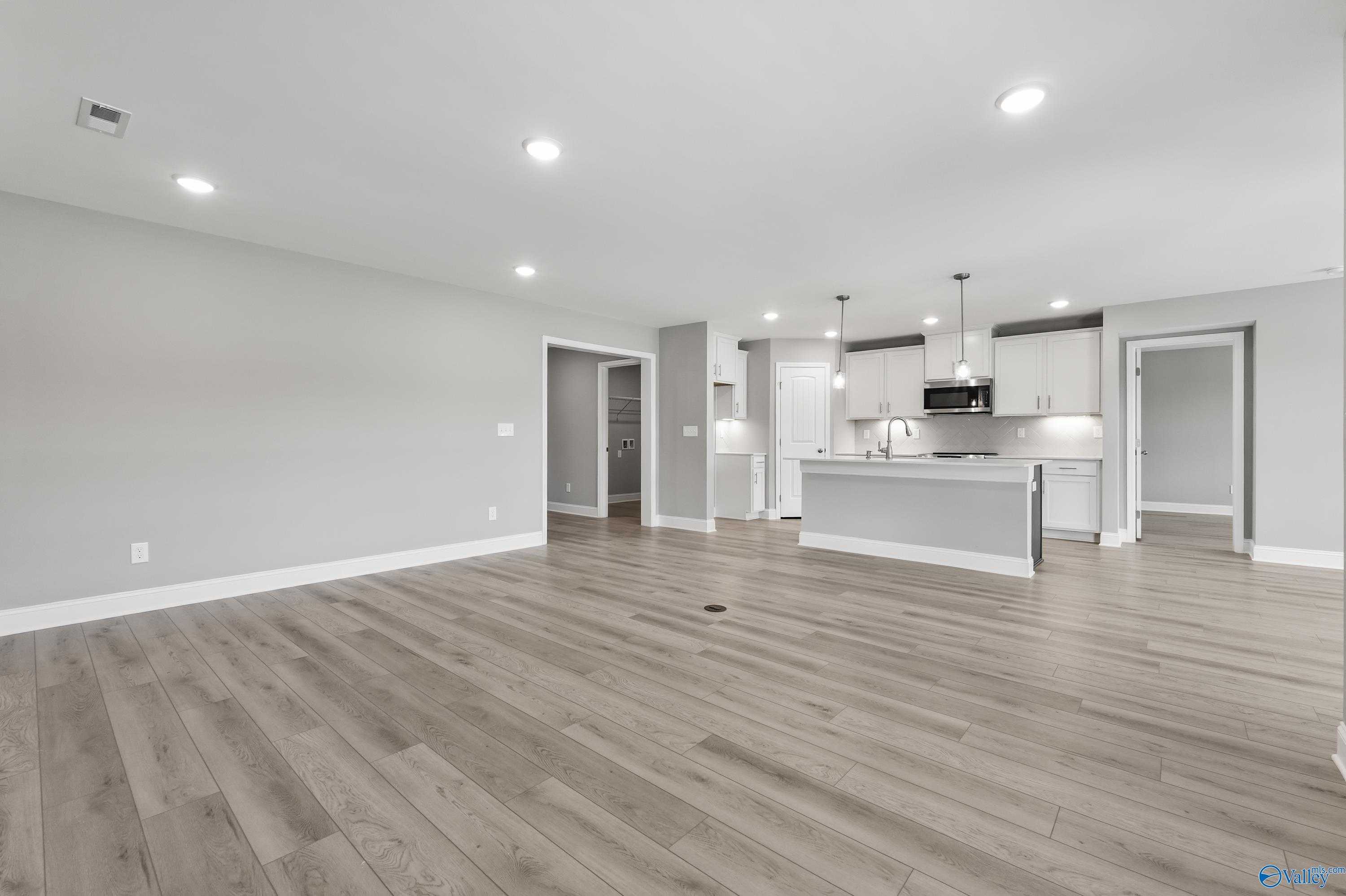 Open-concept kitchen and living space with white cabinets, stainless appliances, hardwood floors in The Everett B, Athens, AL