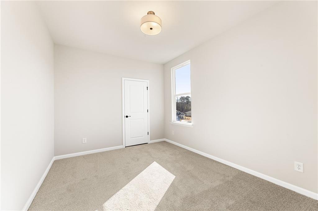 Bright empty secondary bedroom with beige carpet, large sunny window, and neutral walls in Davidson Homes The Glenwood C, Loganville, GA