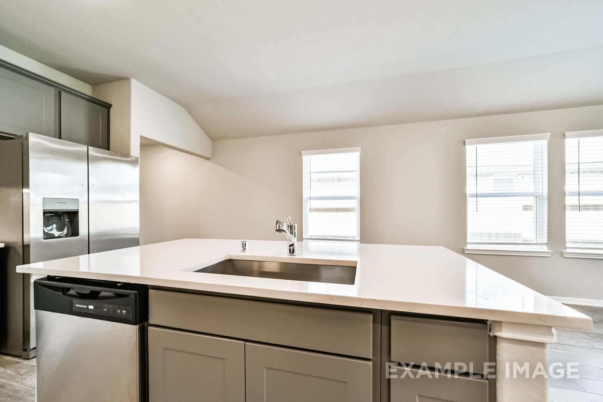 Modern kitchen island with white quartz countertops and stainless steel sink in The Riviera A home at Emberly, Beasley.