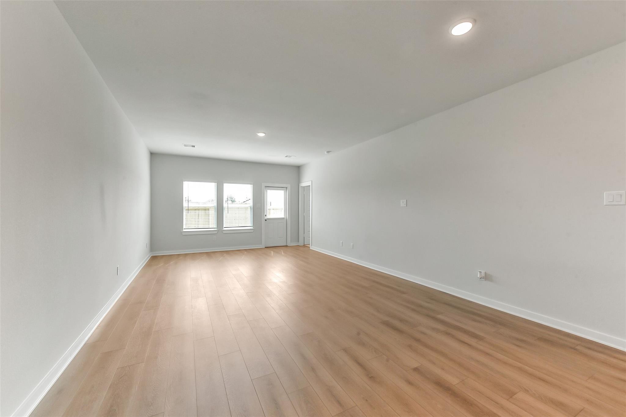 Bright open living room with light hardwood floors, large triple windows, and white walls in Davidson Homes The Sabine F, Dayton Texas