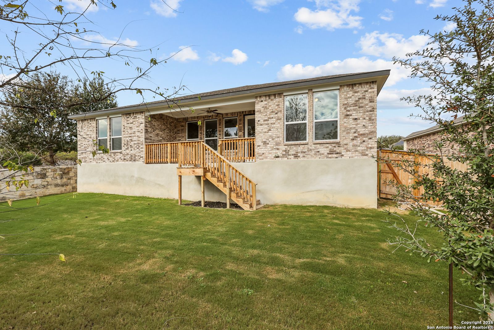 Brick single-story home with covered porch, wooden stairs, large windows, and green lawn in Ladera, San Antonio, Texas