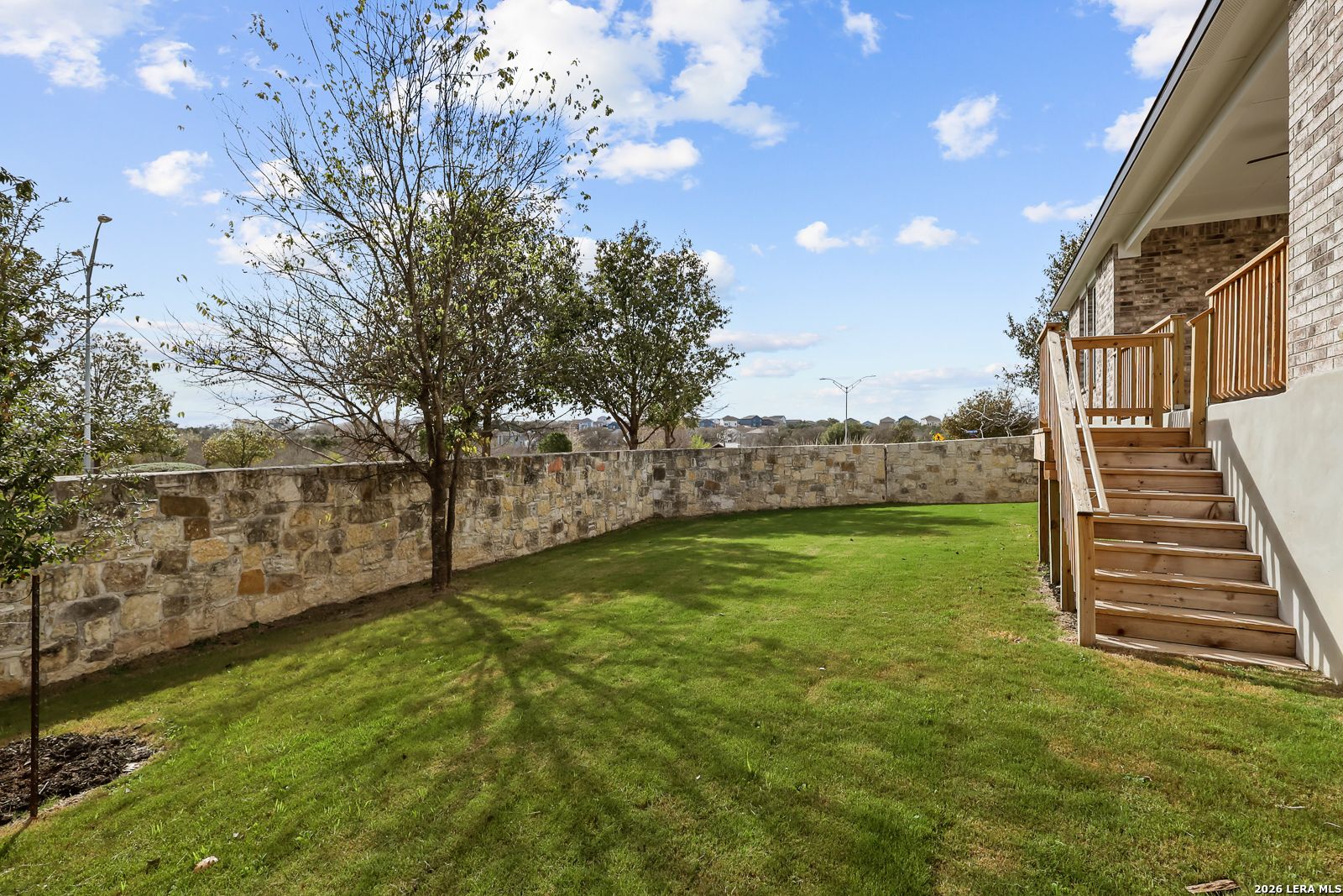 Private backyard with stone wall and wooden deck stairs at a Davidson Homes Lanier H floor plan in Ladera, San Antonio.