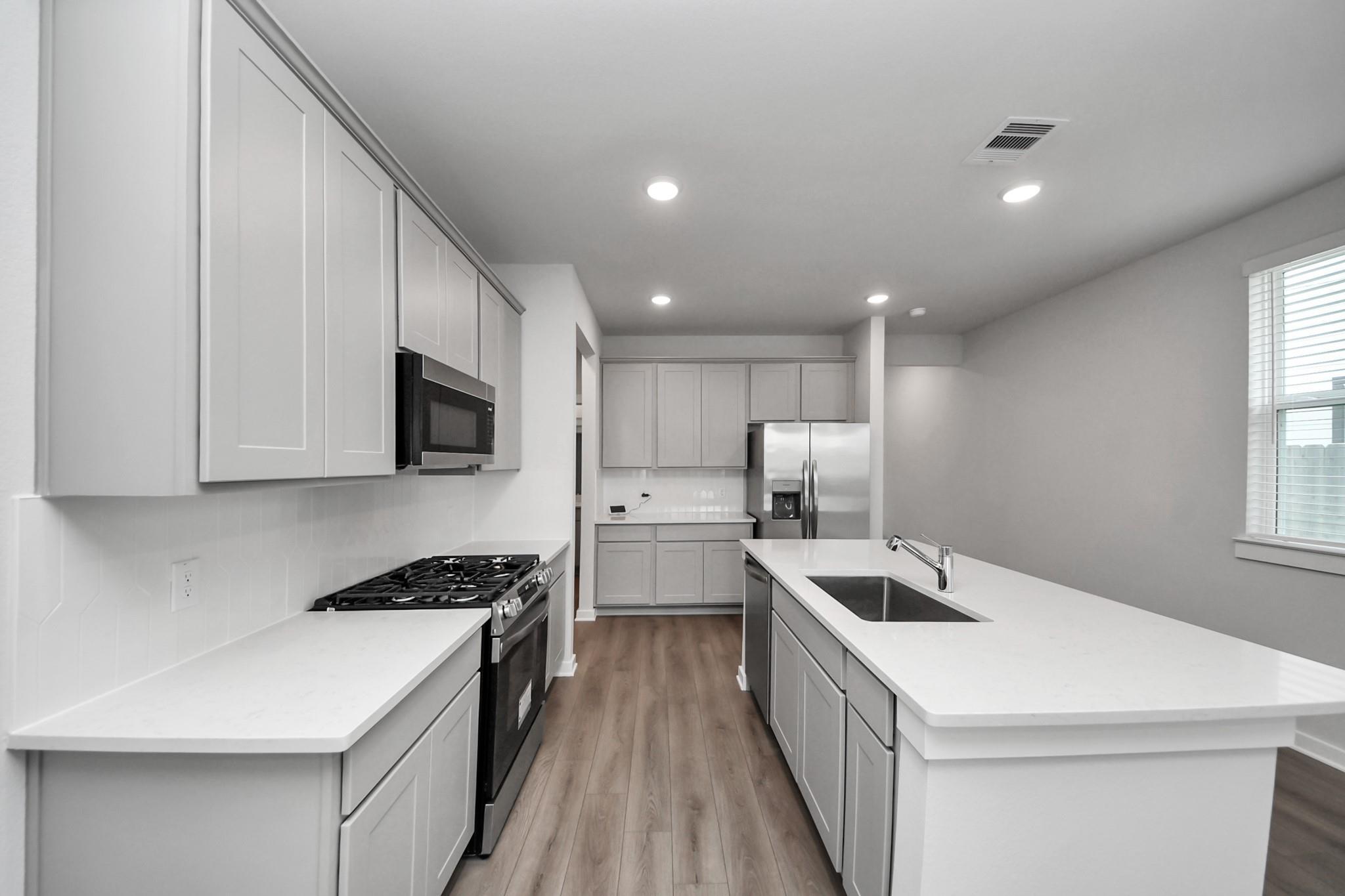 Modern kitchen with white cabinetry, quartz countertops, island sink, and stainless appliances in Davidson Homes The Frio F, Houston