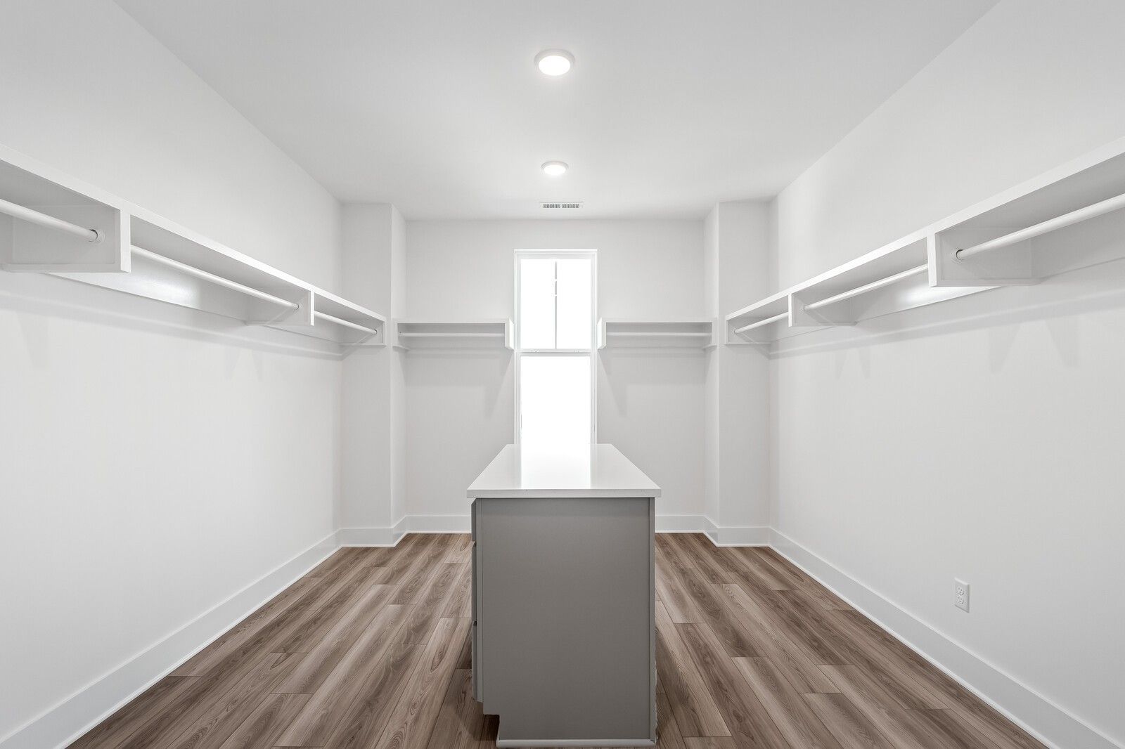 Spacious walk-in closet with built-in white shelving, gray center island, and window in Davidson Homes The Alston A, Murfreesboro, TN