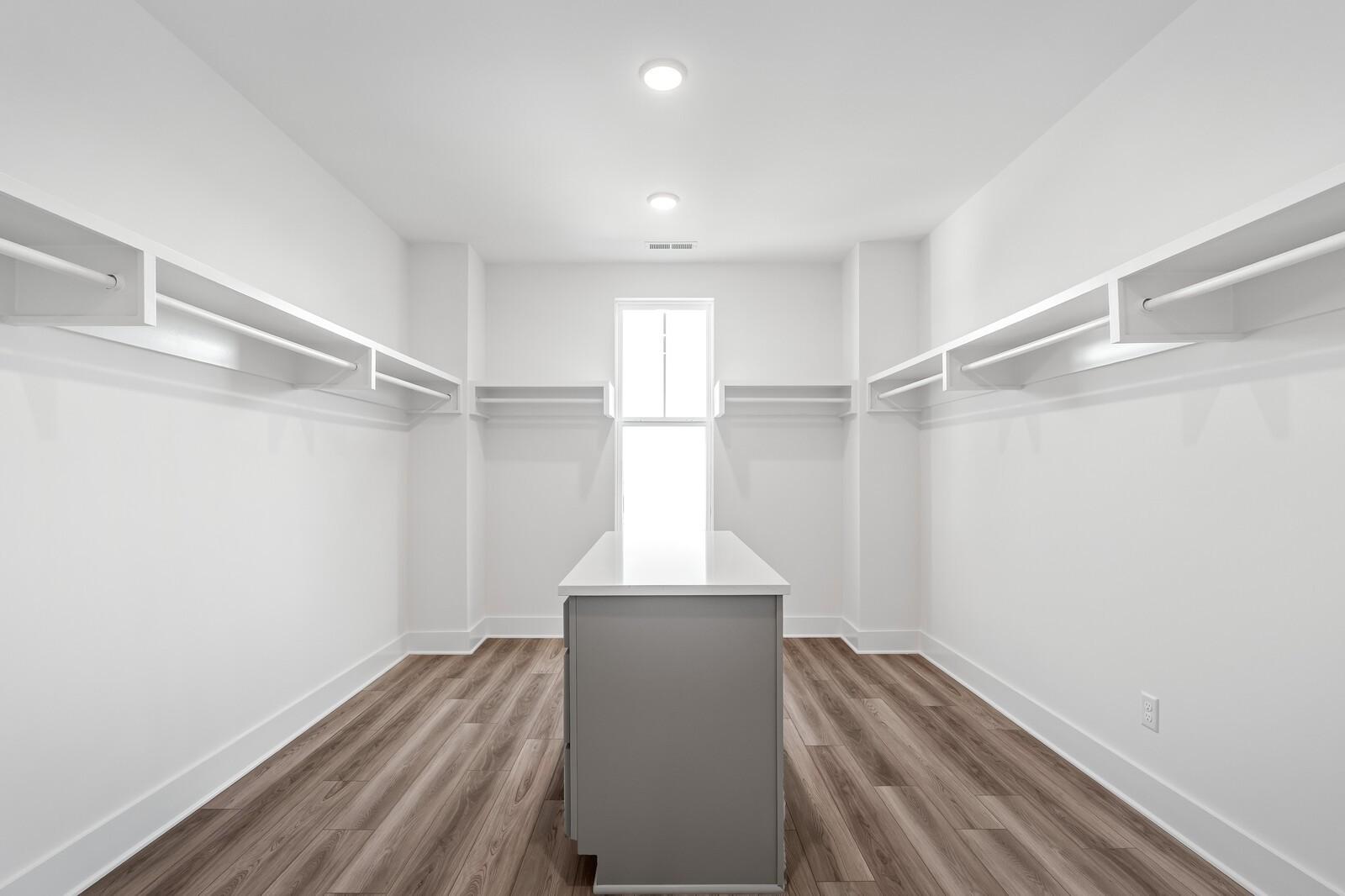 Spacious walk-in closet with built-in white shelving, gray center island, and window in Davidson Homes The Alston A, Murfreesboro, TN