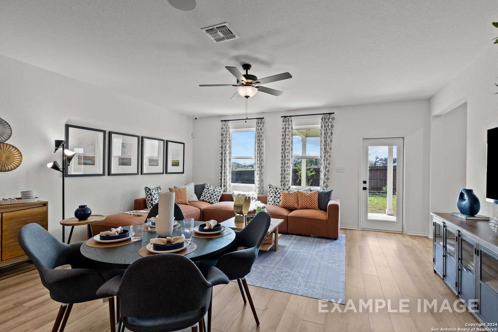 Open-concept living room with orange sofa, round dining table, ceiling fan, and backyard views in The Douglas G, Bricewood, San Antonio