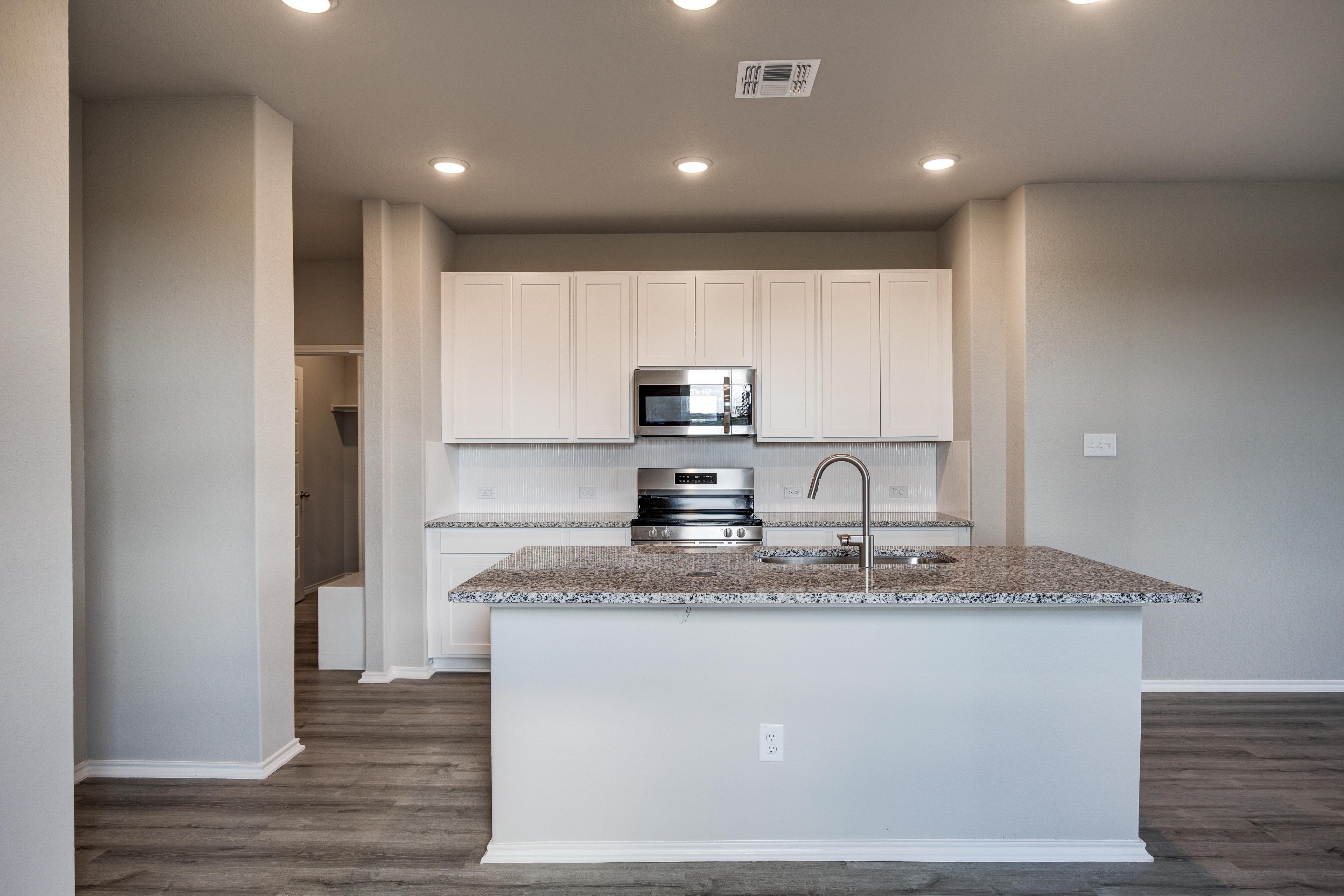 Spacious Blanco C kitchen with white shaker cabinets, granite island sink, stainless microwave, oven, and hardwood floors