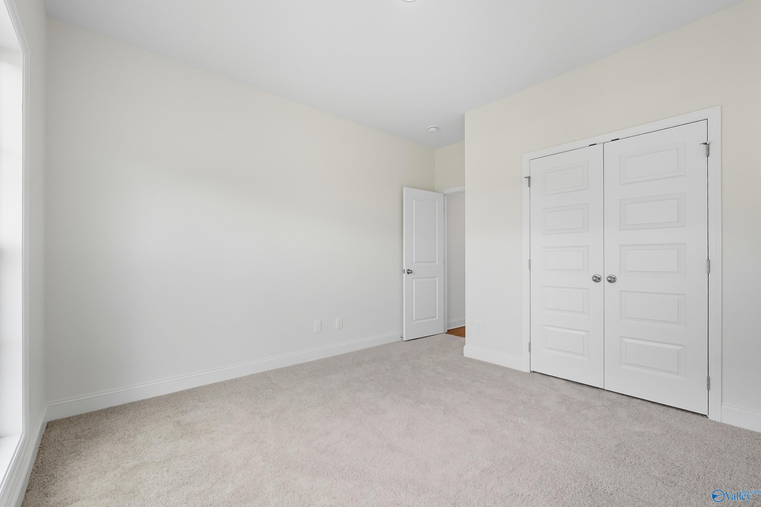 Bright secondary bedroom featuring neutral walls, plush carpet, double closet doors, and window light in Davidson Homes The Everett, Meridianville, Alabama