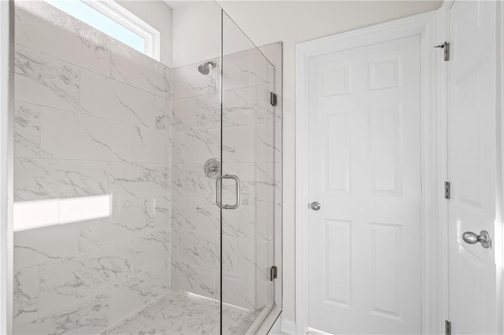 Walk-in shower with marble-style tile and glass door in The Glenwood A floor plan at Wehunt Meadows, Hoschton, Georgia.