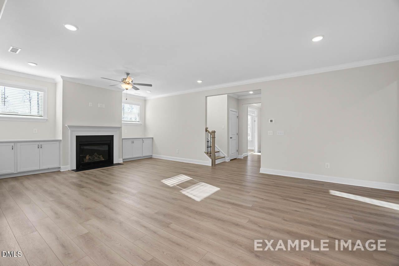 Spacious family room featuring gas fireplace, built-in cabinets, ceiling fan, and open staircase in Davidson Homes The Aspen C, Apex, NC