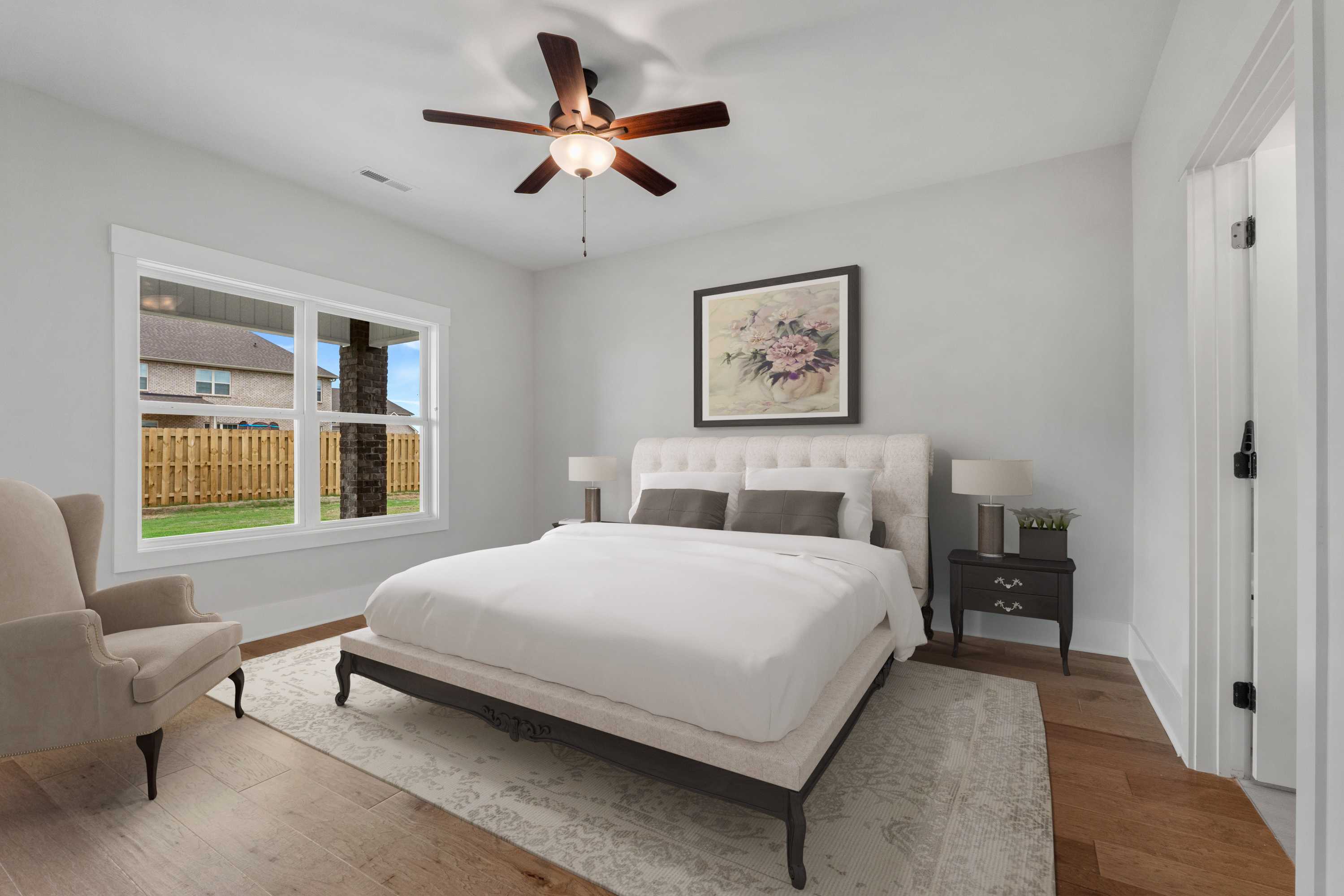 Spacious master bedroom at The Villas at Barnett's Crossing in Madison AL with king bed, ceiling fan, hardwood floors, and backyard view