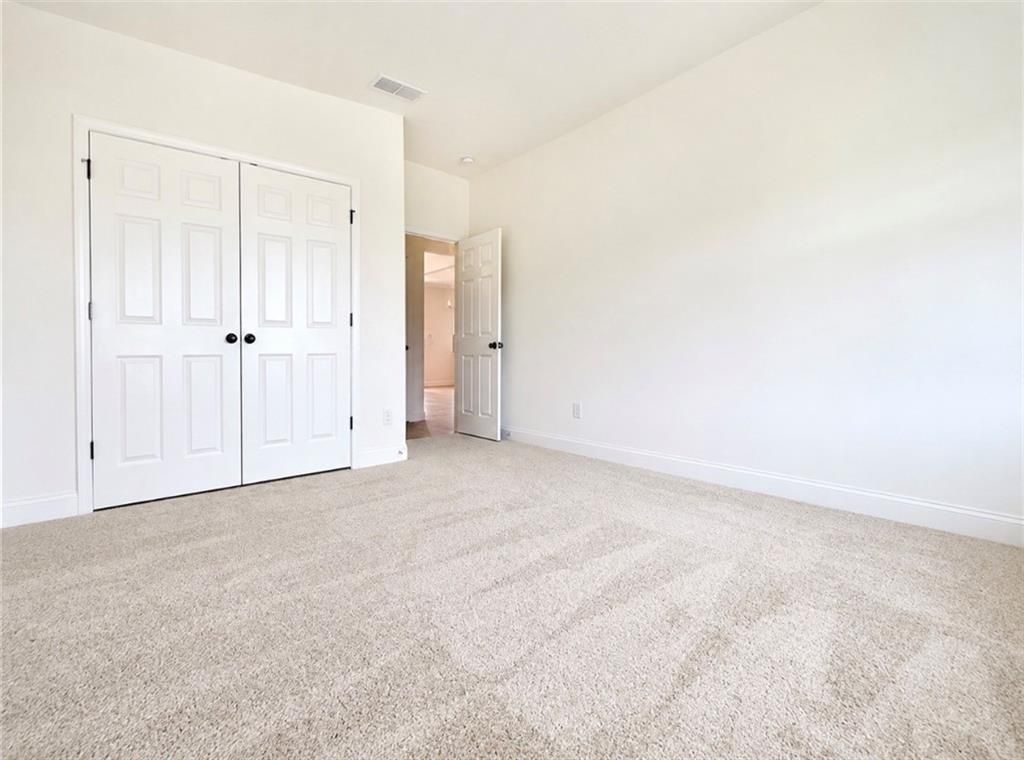 Spacious secondary bedroom with neutral carpet and walk-in closet in The Hickory C floor plan, Wehunt Meadows, Hoschton, GA.