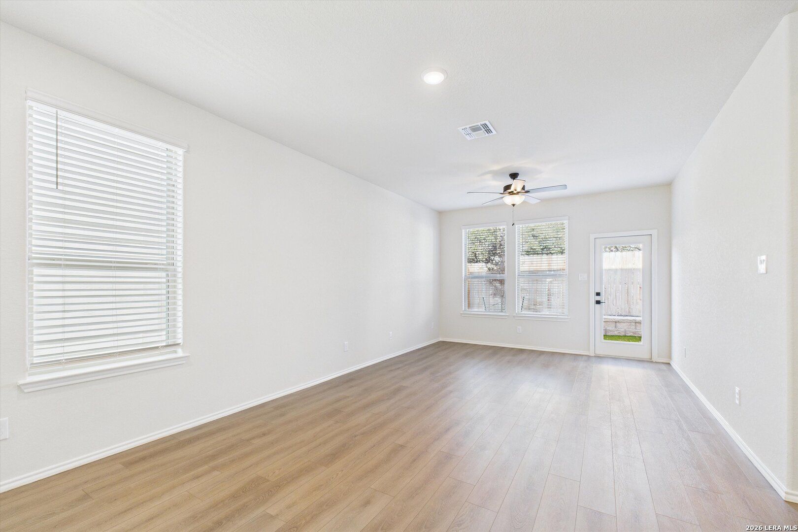 Empty family room with light hardwood floors, beige walls, ceiling fan, and sliding door to backyard in Davidson Homes The Gillian B, San Antonio