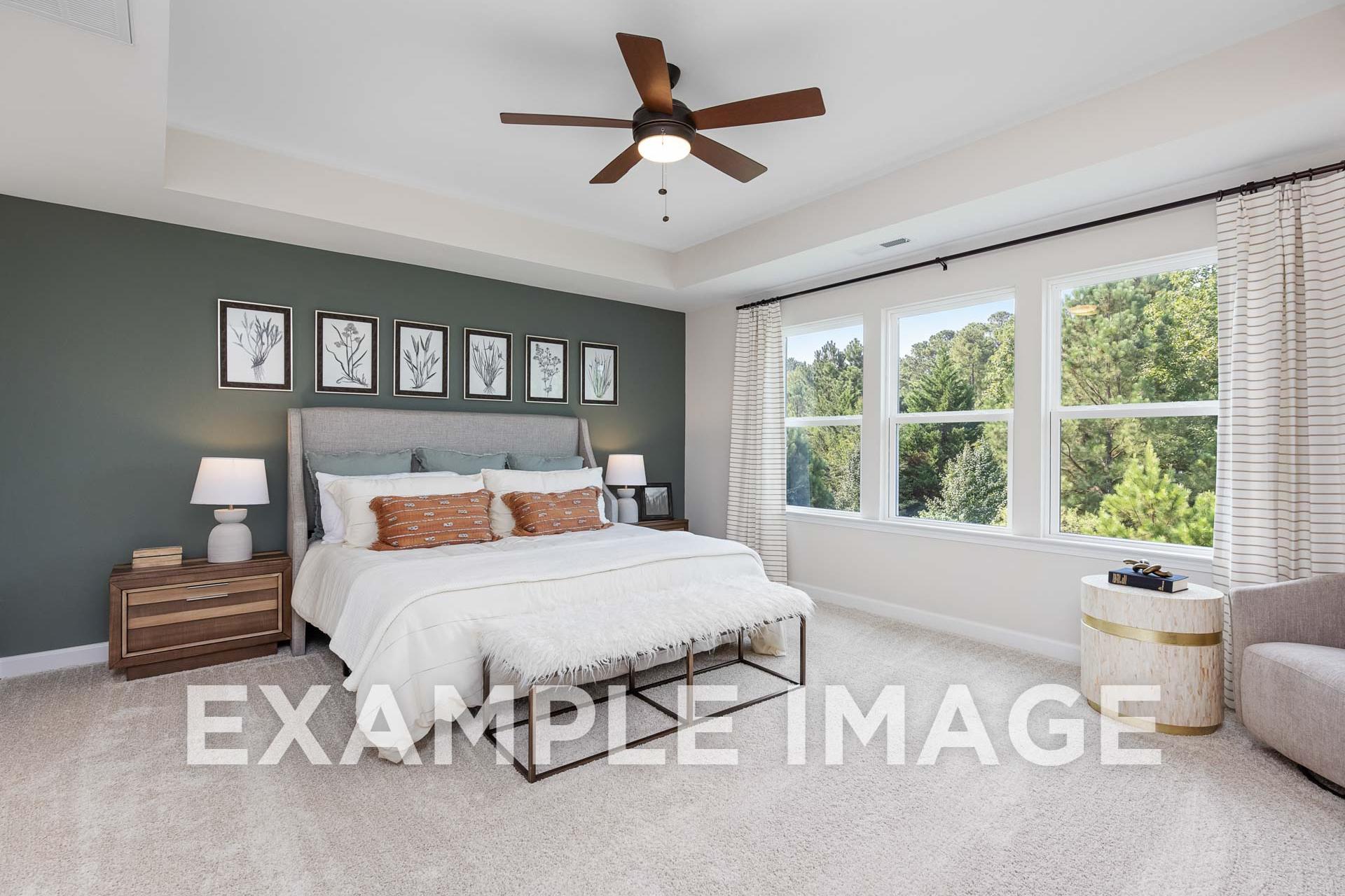 Spacious master bedroom in The Willow E with king bed, ceiling fan, large tree-view windows, green accent wall and plush armchair