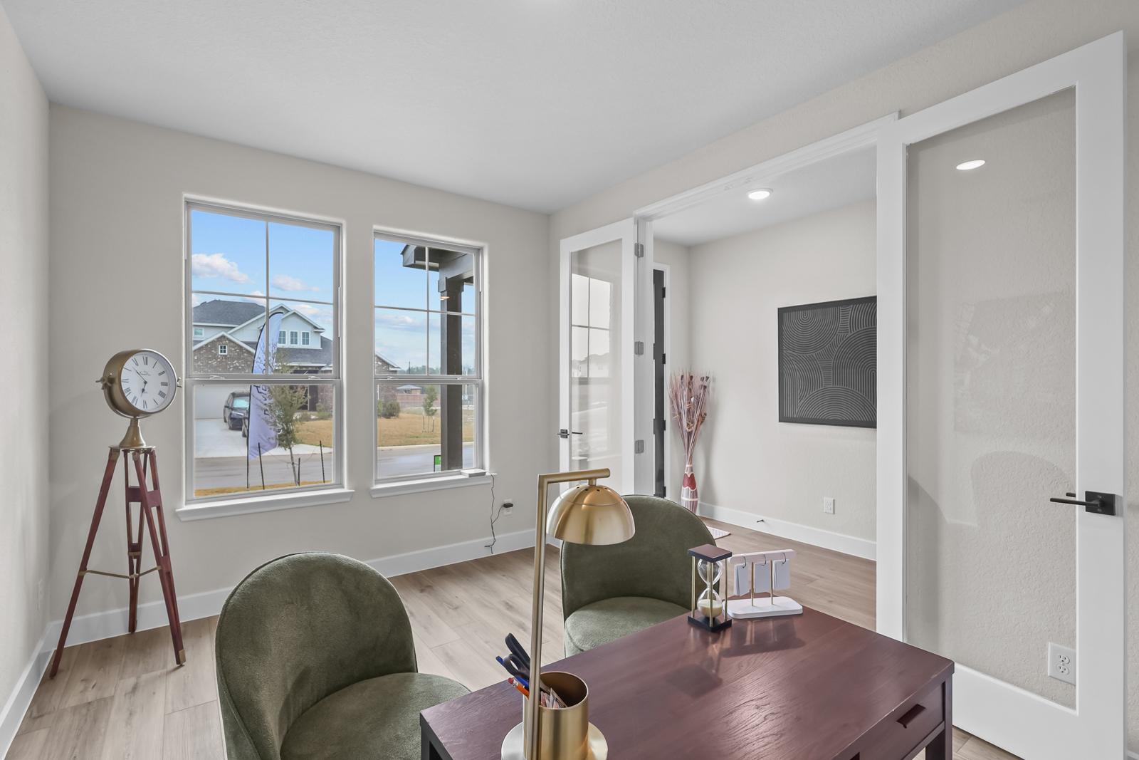 Modern home office in The Belmont J floor plan featuring glass French doors, wood-look flooring, and a bright workspace.