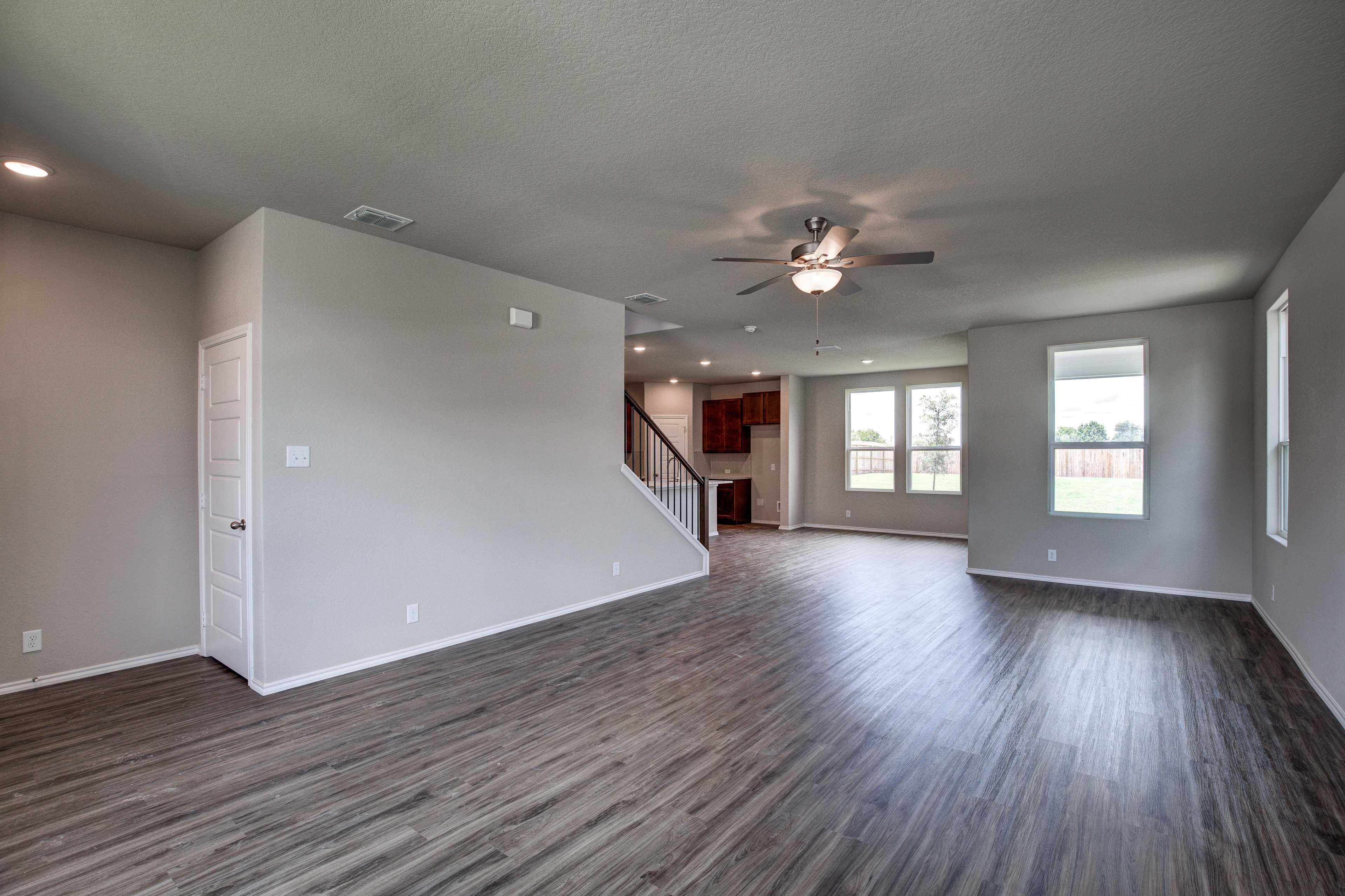 Open-concept living area in The Murray home with dark hardwood floors, ceiling fans, large windows, and staircase to upper level