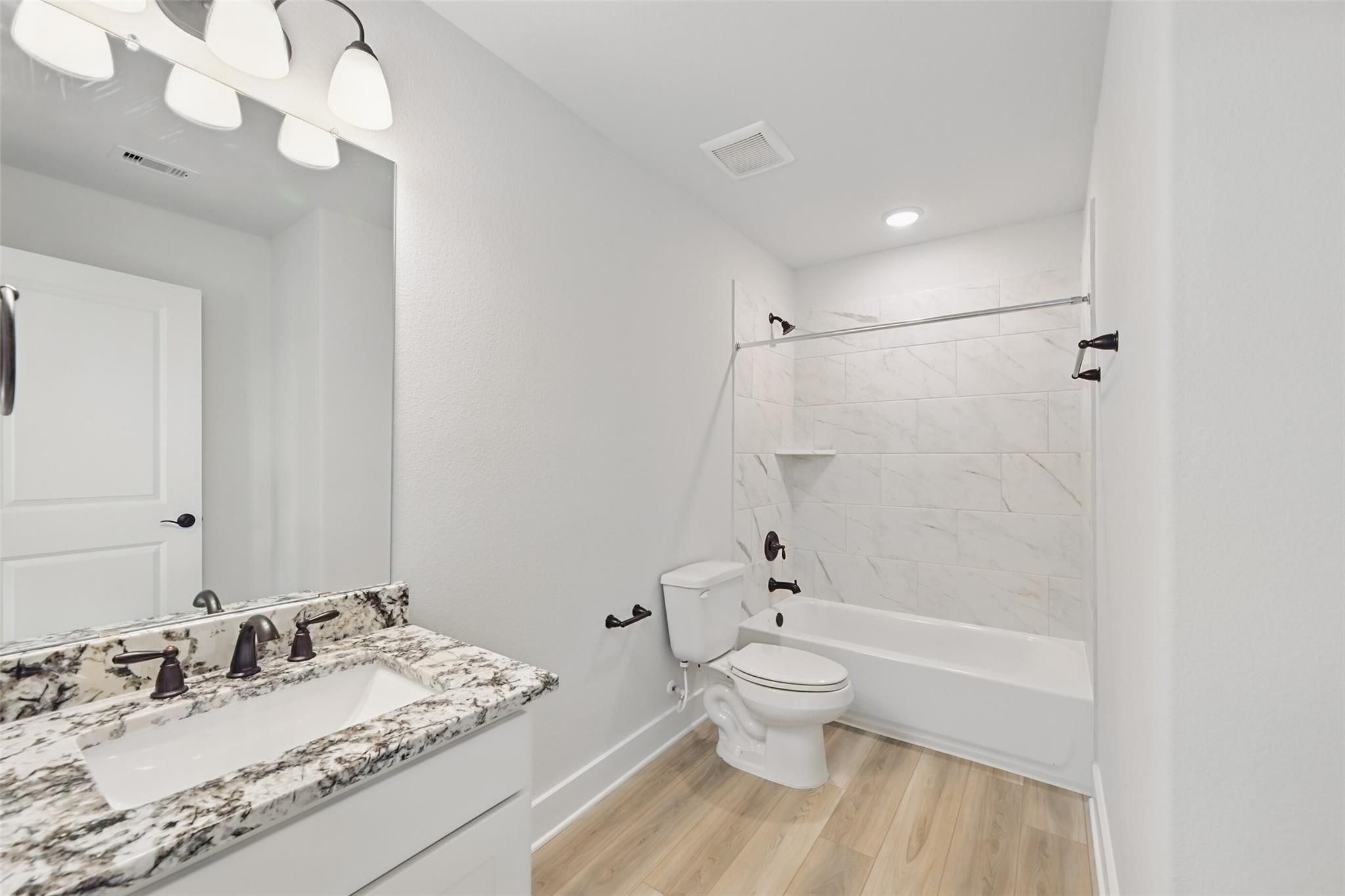 Modern bathroom featuring white subway tile tub-shower combo, double marble vanity, and hardwood floors in Davidson Homes The Victoria C, Lago Mar, Texas City