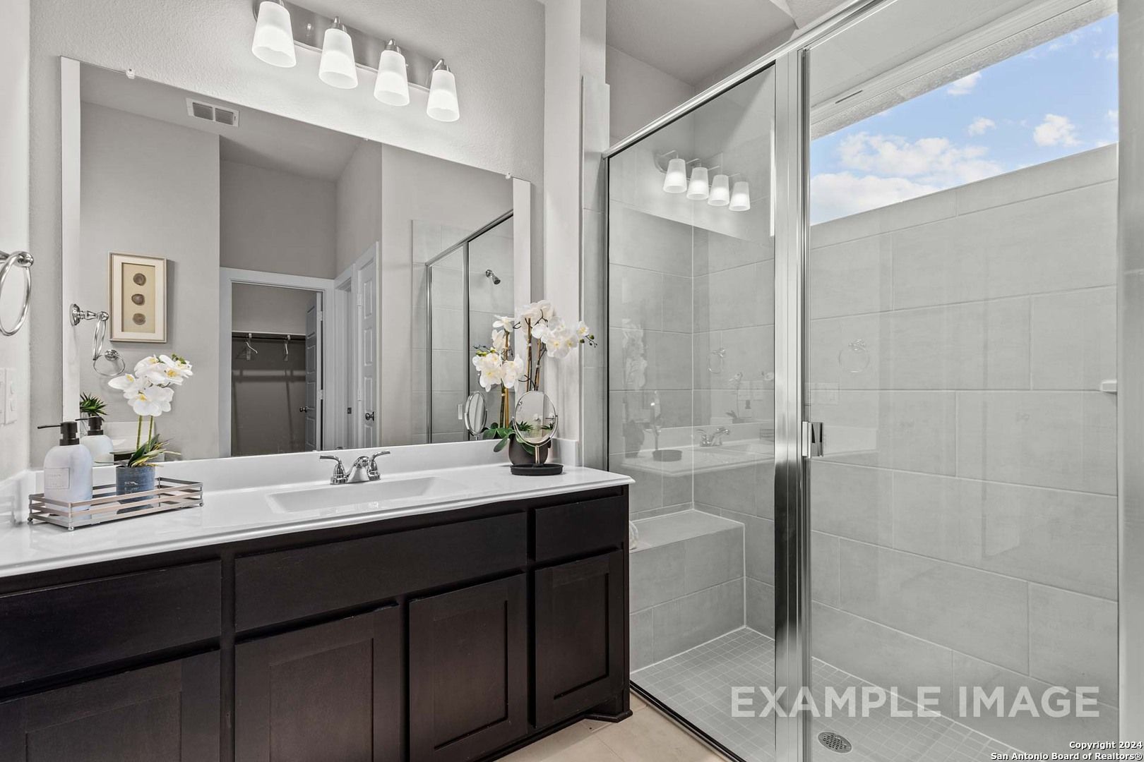 Elegant master bathroom with dark wood vanity, frameless glass shower, orchids, and natural light in Davidson Homes The Collin A, Seguin, Texas