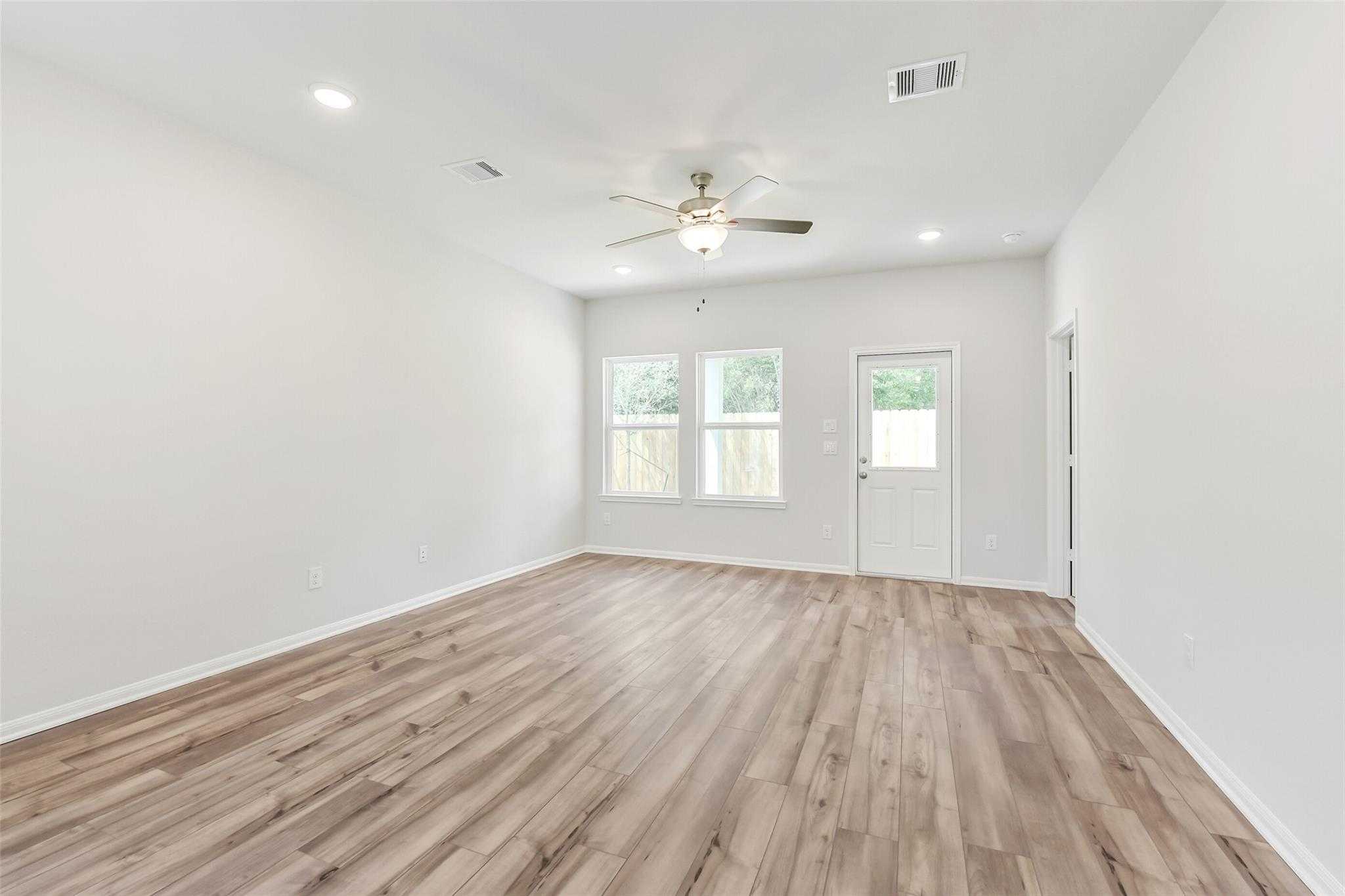Spacious living room featuring hardwood floors, ceiling fan, large windows, and French doors in Davidson Homes The Sabine E, Conroe, Texas