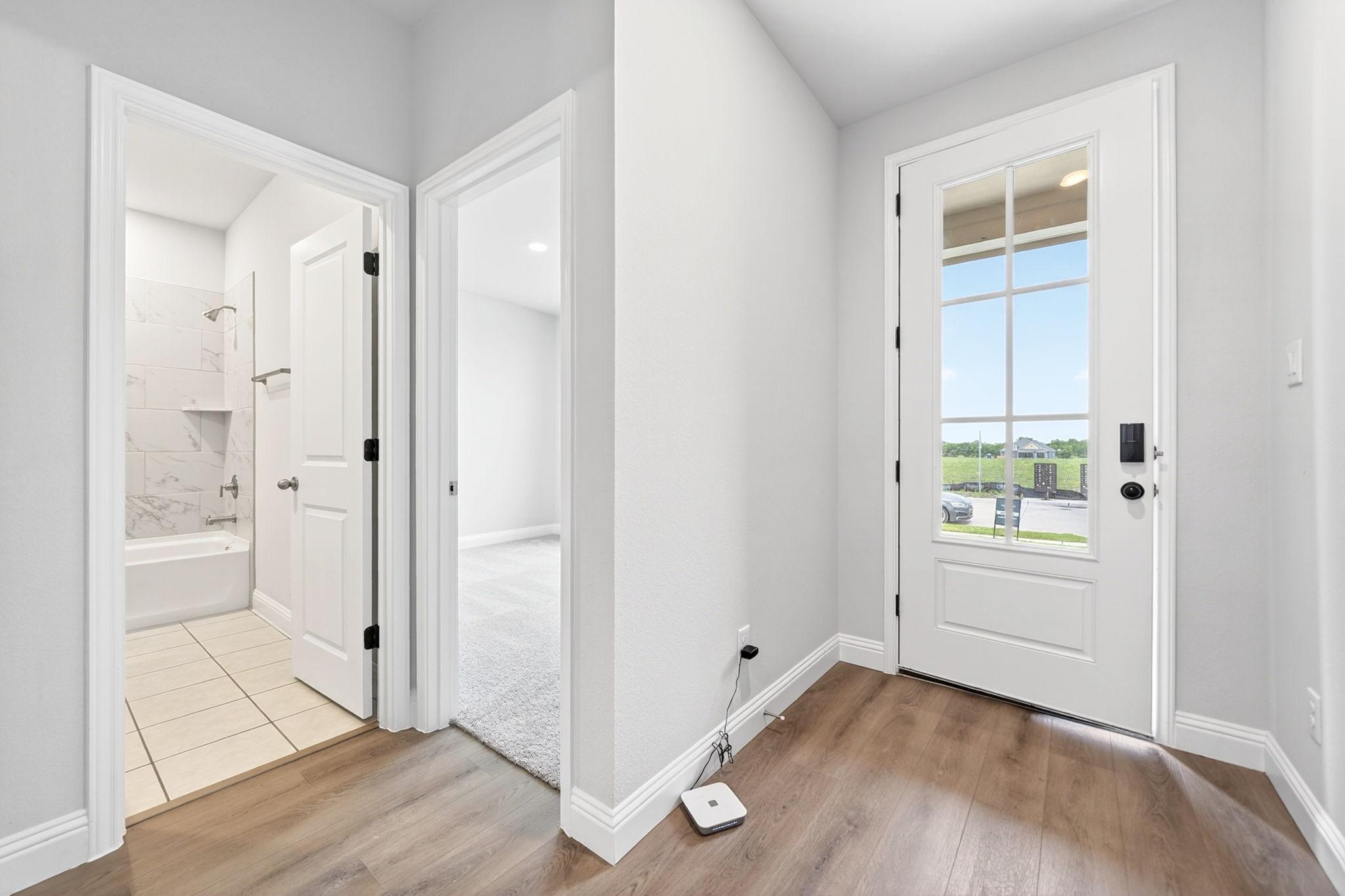 Entryway and interior layout of The Redbud home design featuring wood-look flooring, guest bathroom, and bedroom access.