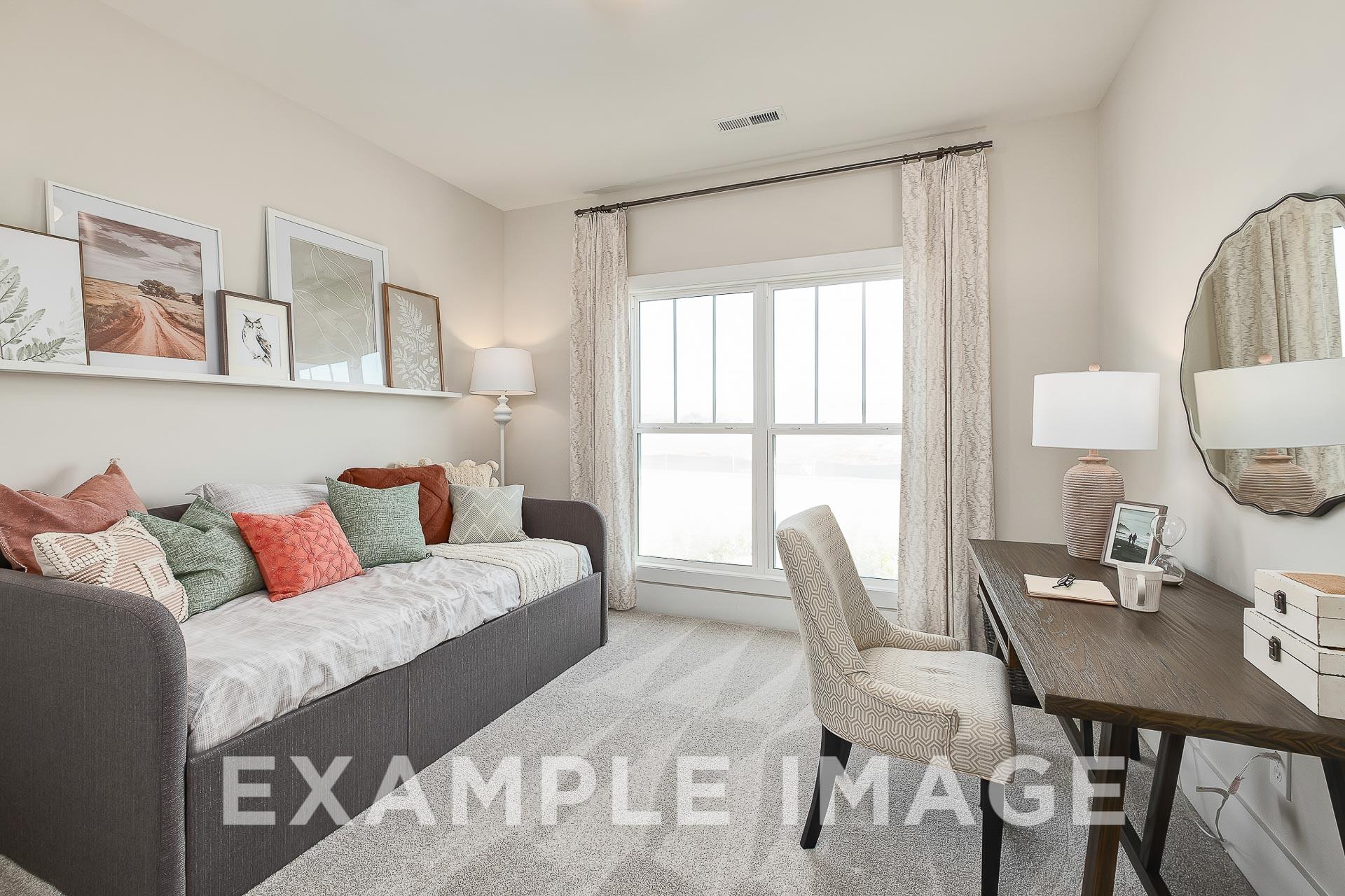 Cozy home office in The Everett B with gray daybed, colorful pillows, wooden desk, and large sunlit window